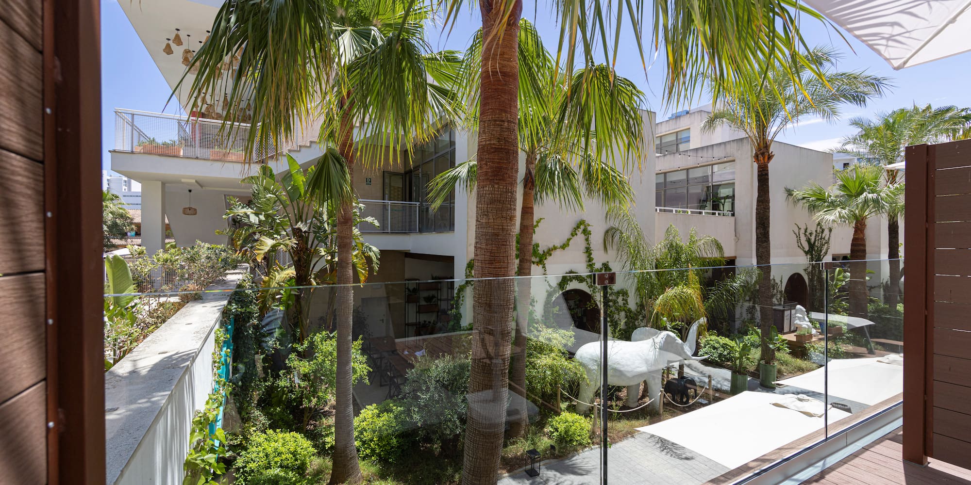 Balcony view: Modern tropical hotel courtyard with palm trees and white elephant.