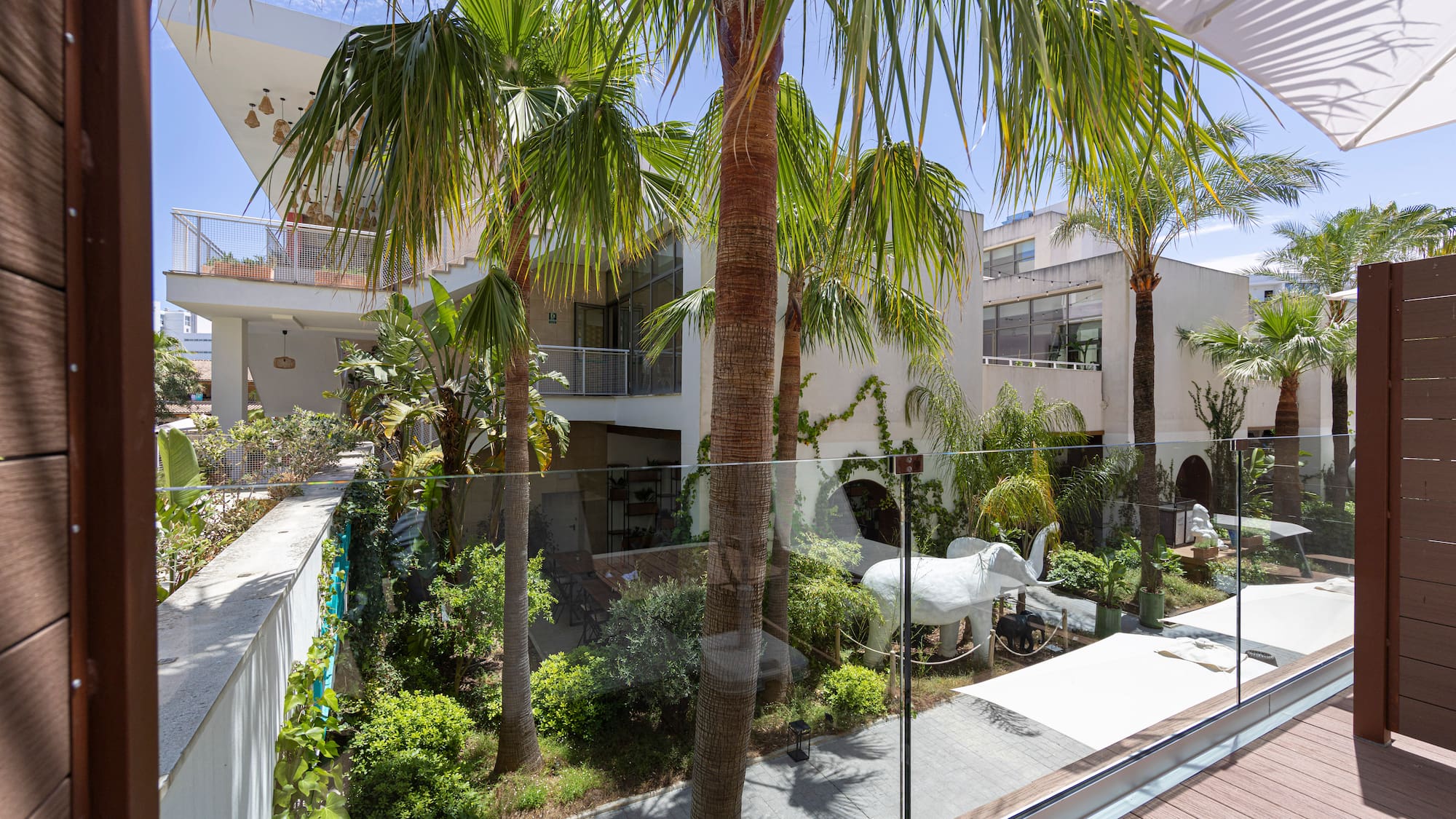 Balcony view: Modern tropical hotel courtyard with palm trees and white elephant.