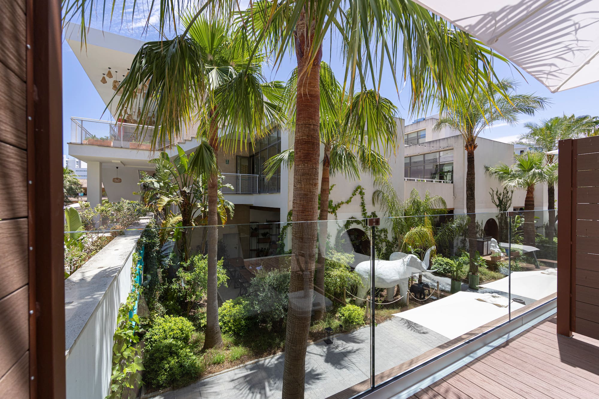 Balcony view: Modern tropical hotel courtyard with palm trees and white elephant.