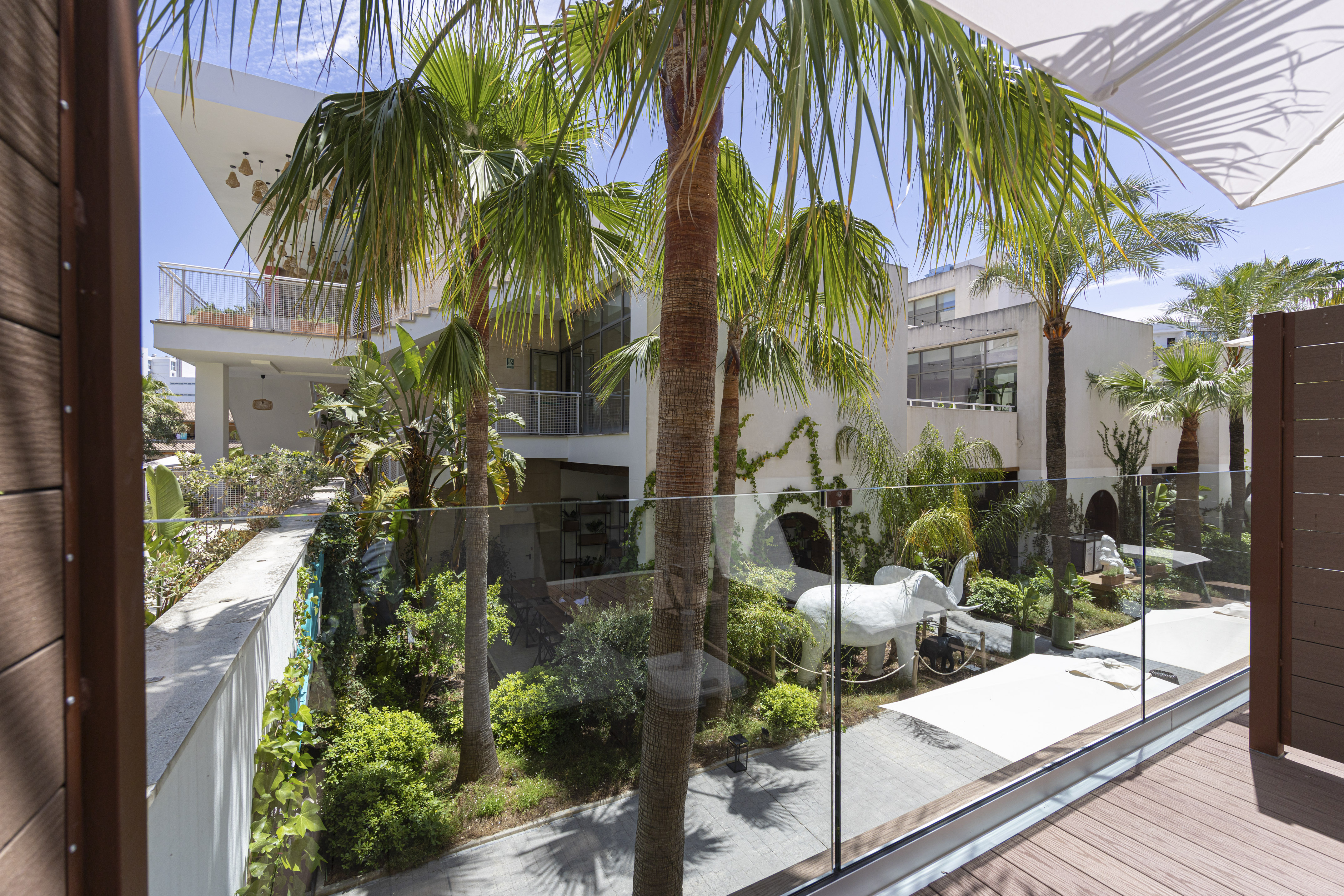 Balcony view: Modern tropical hotel courtyard with palm trees and white elephant.