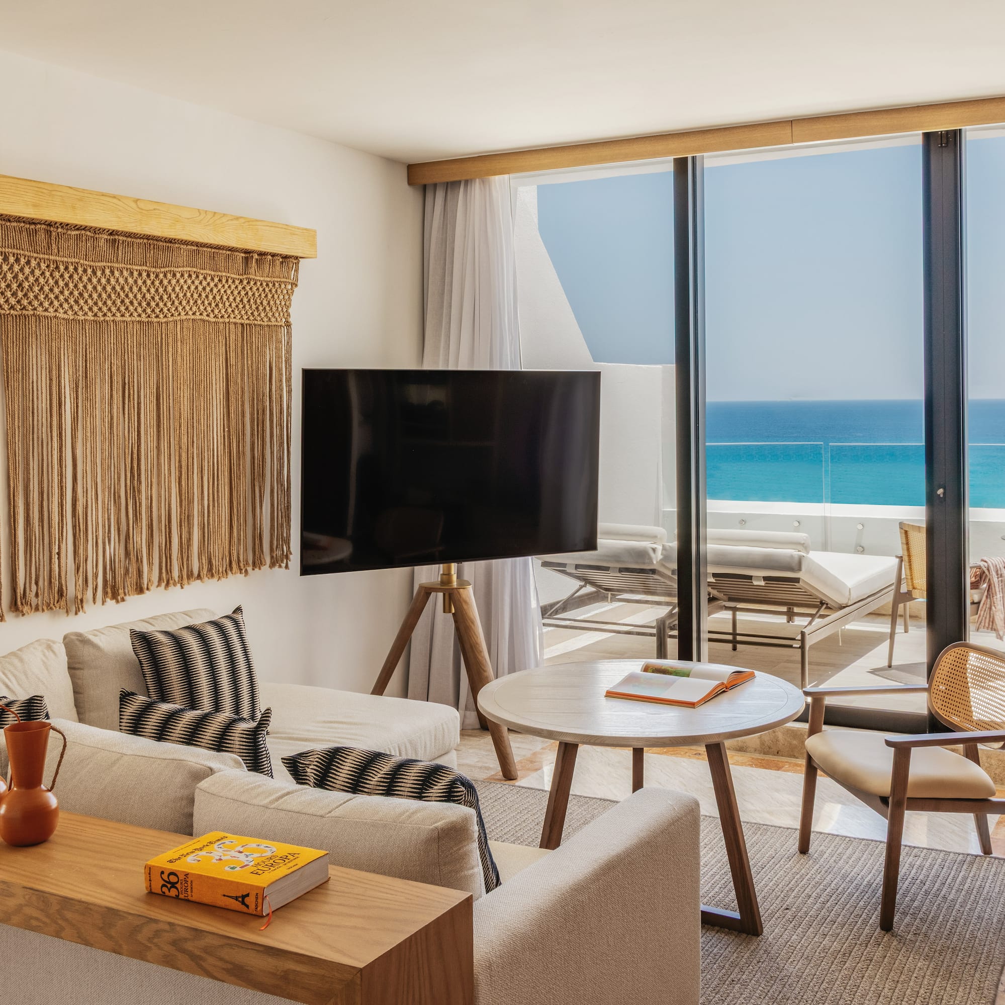 Ocean view living room with macrame wall art, sofa, and balcony terrace.