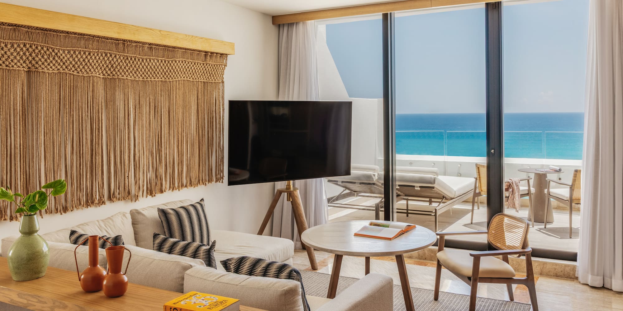 Ocean view living room with macrame wall art, sofa, and balcony terrace.