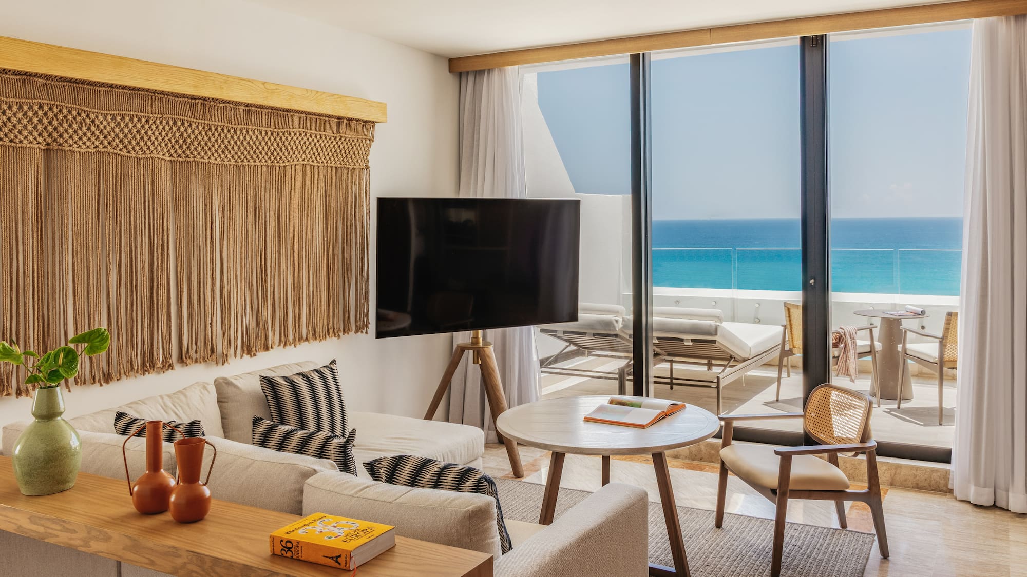 Ocean view living room with macrame wall art, sofa, and balcony terrace.