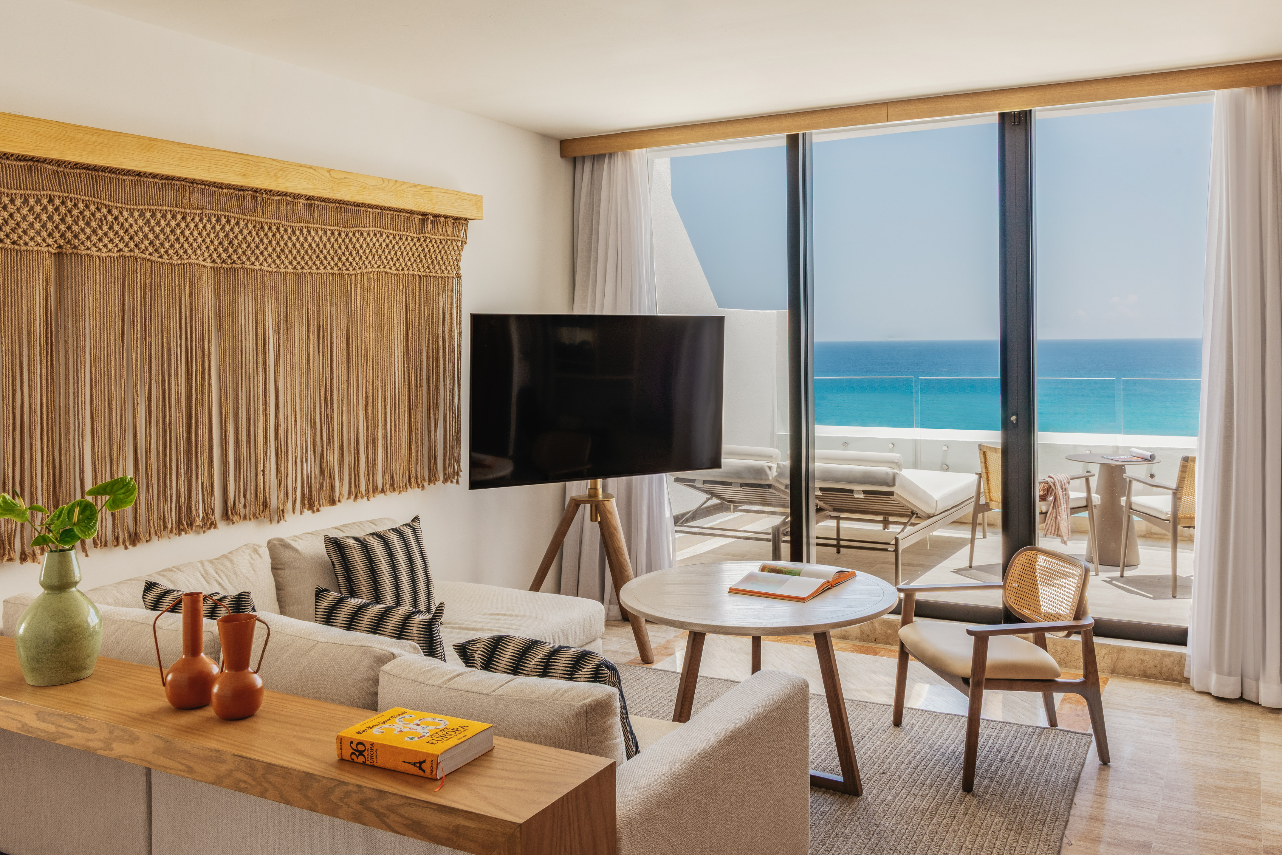 Ocean view living room with macrame wall art, sofa, and balcony terrace.