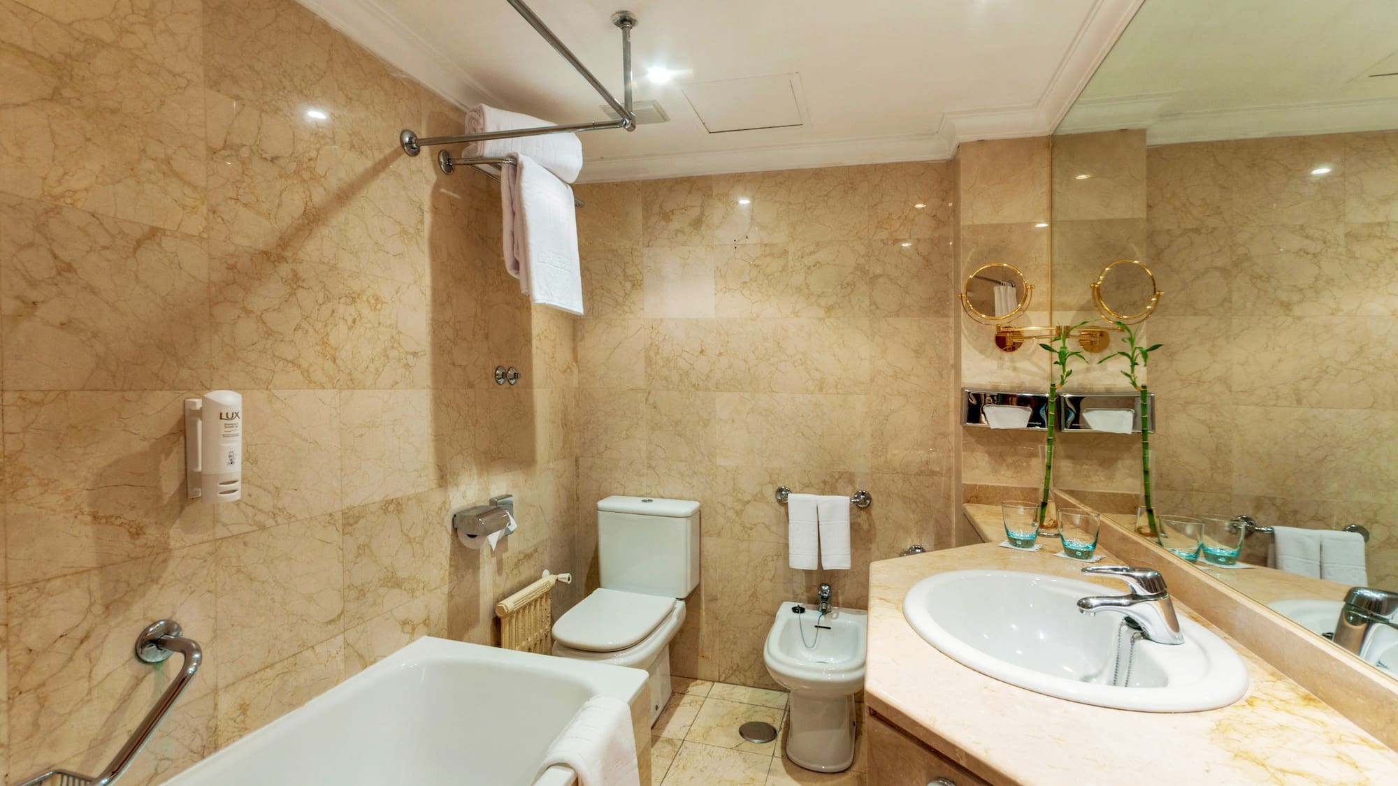 Marble hotel bathroom with bathtub, toilet, bidet, and vanity sink.