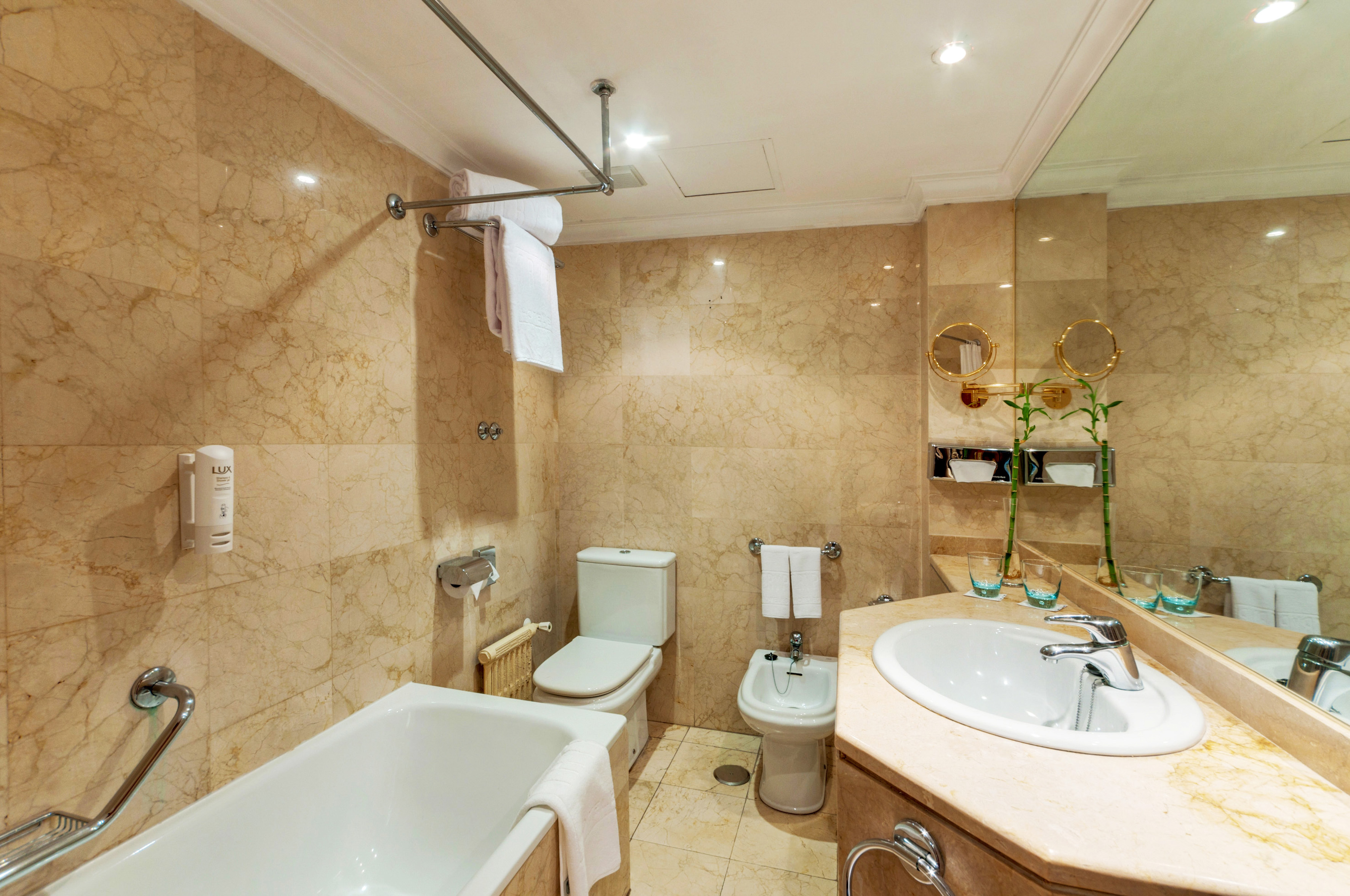 Marble hotel bathroom with bathtub, toilet, bidet, and vanity sink.