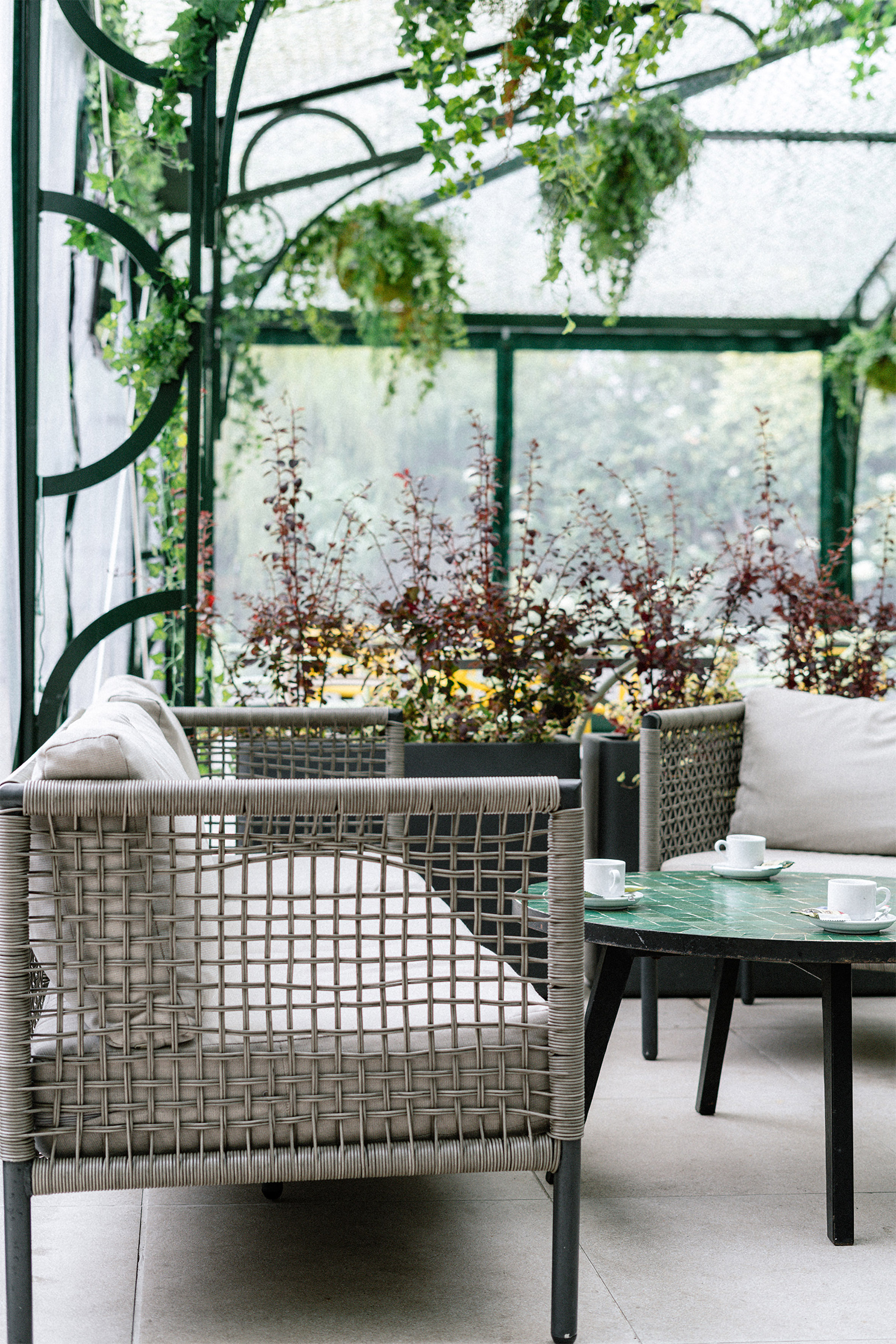 Cozy conservatory lounge with wicker seating, green table, and lush plants. - Jardín Urbano - Palacio de Avilés Affiliated by Meliá, Avilés