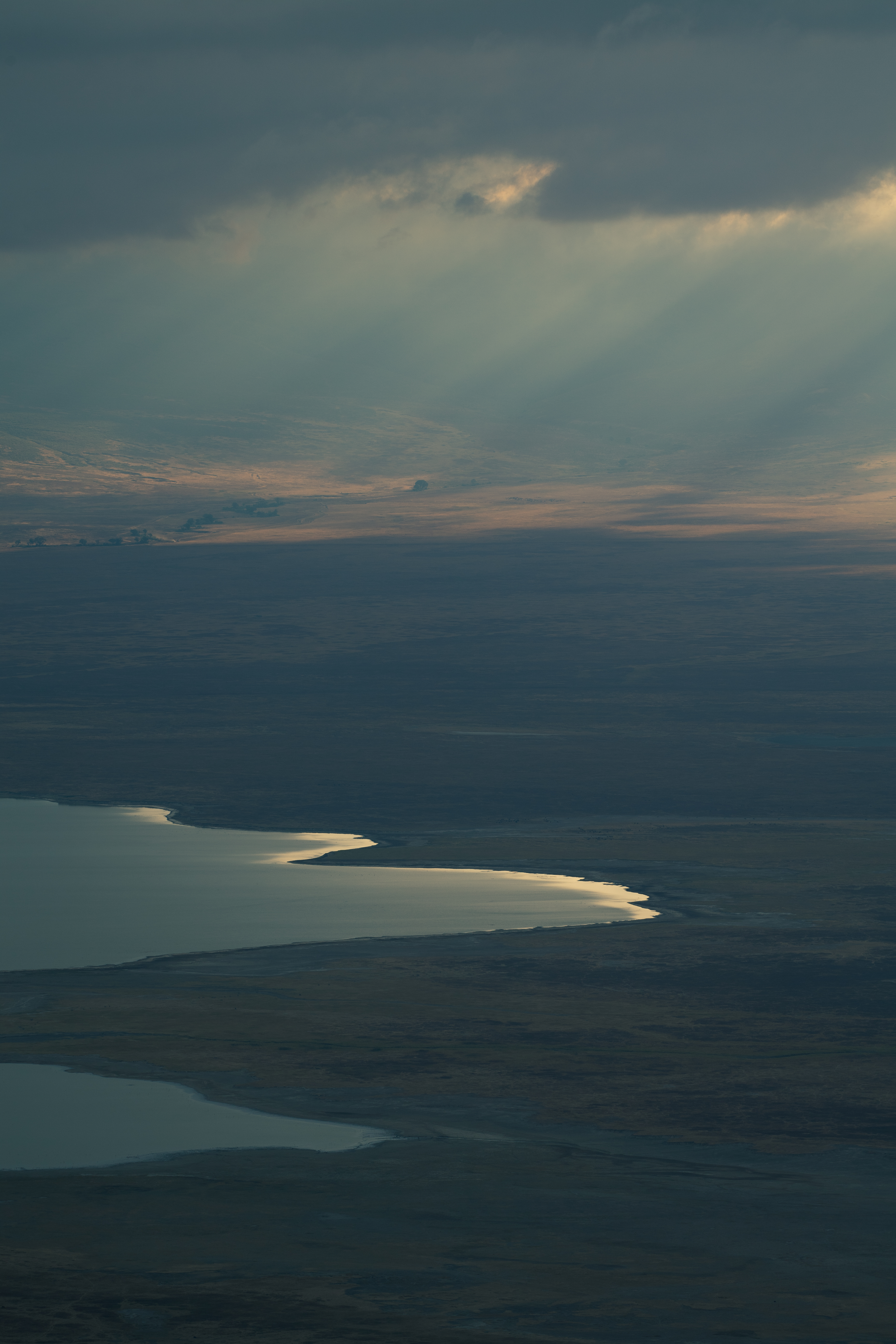 Aerial view of lake reflecting sunbeams through dark clouds.
