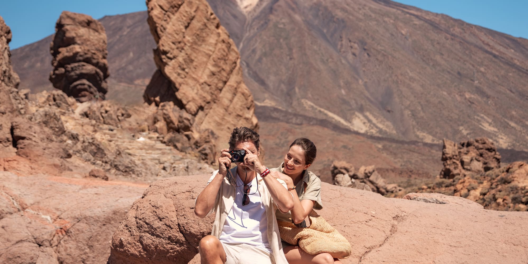 a man and woman sitting on a rock taking a picture of a mountain