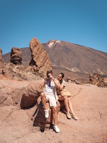 a man and woman sitting on a rock taking a picture of a mountain