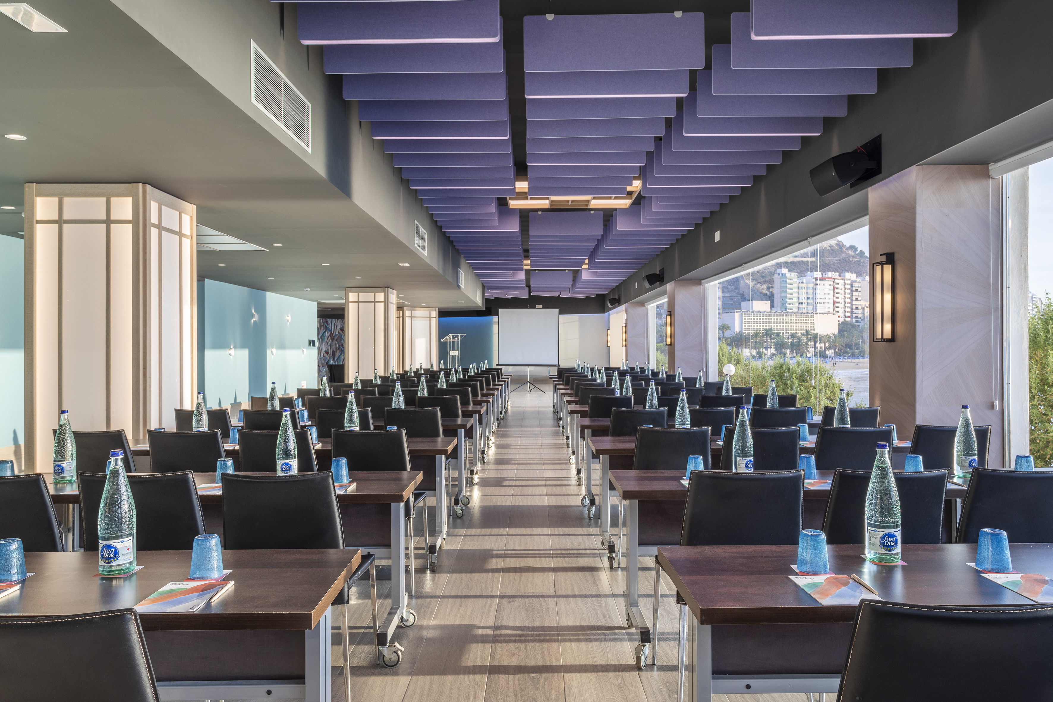 Modern conference room with classroom setup, projector screen, and coastal view.