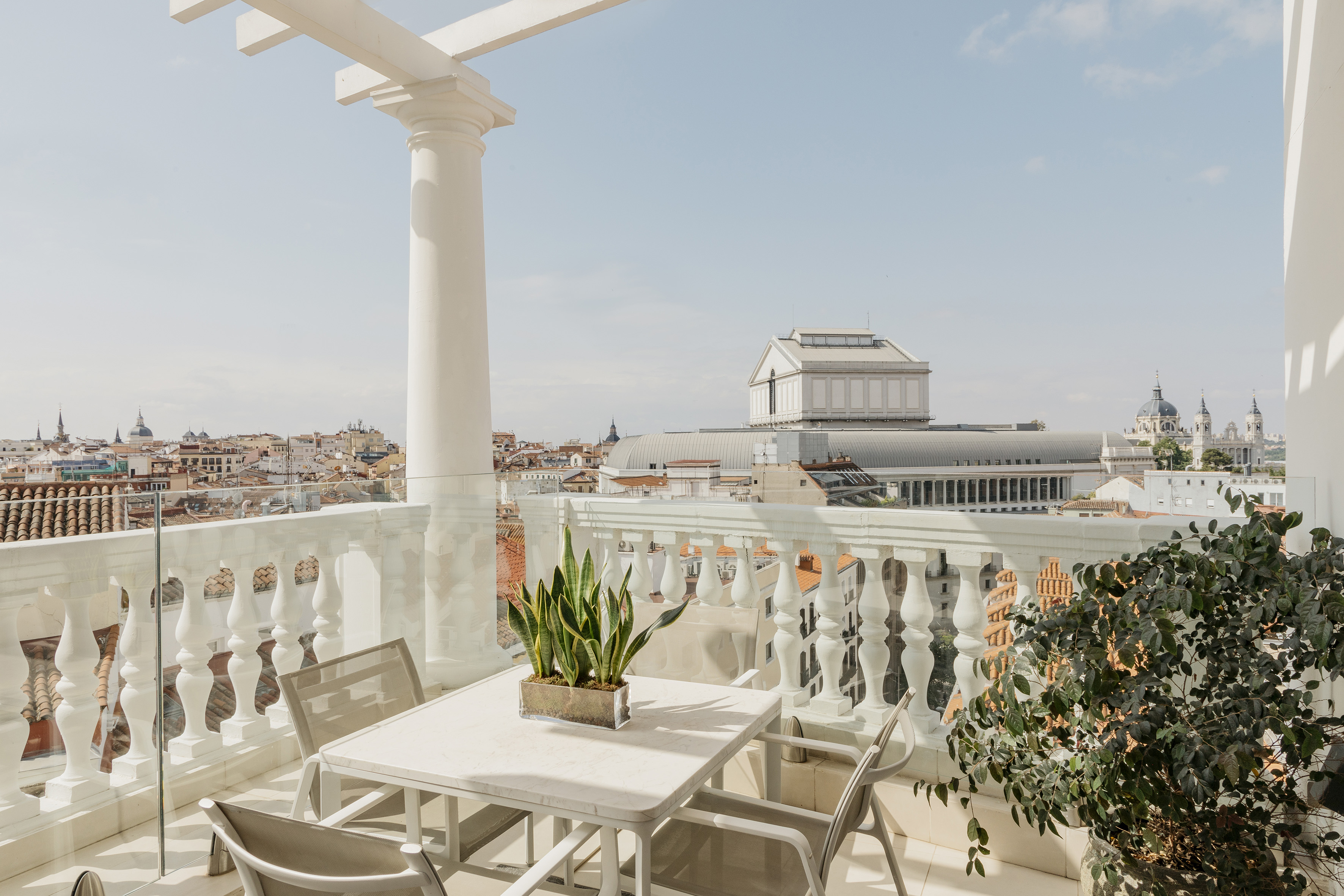 Sunny Madrid rooftop terrace with outdoor table, chairs, and city skyline view.