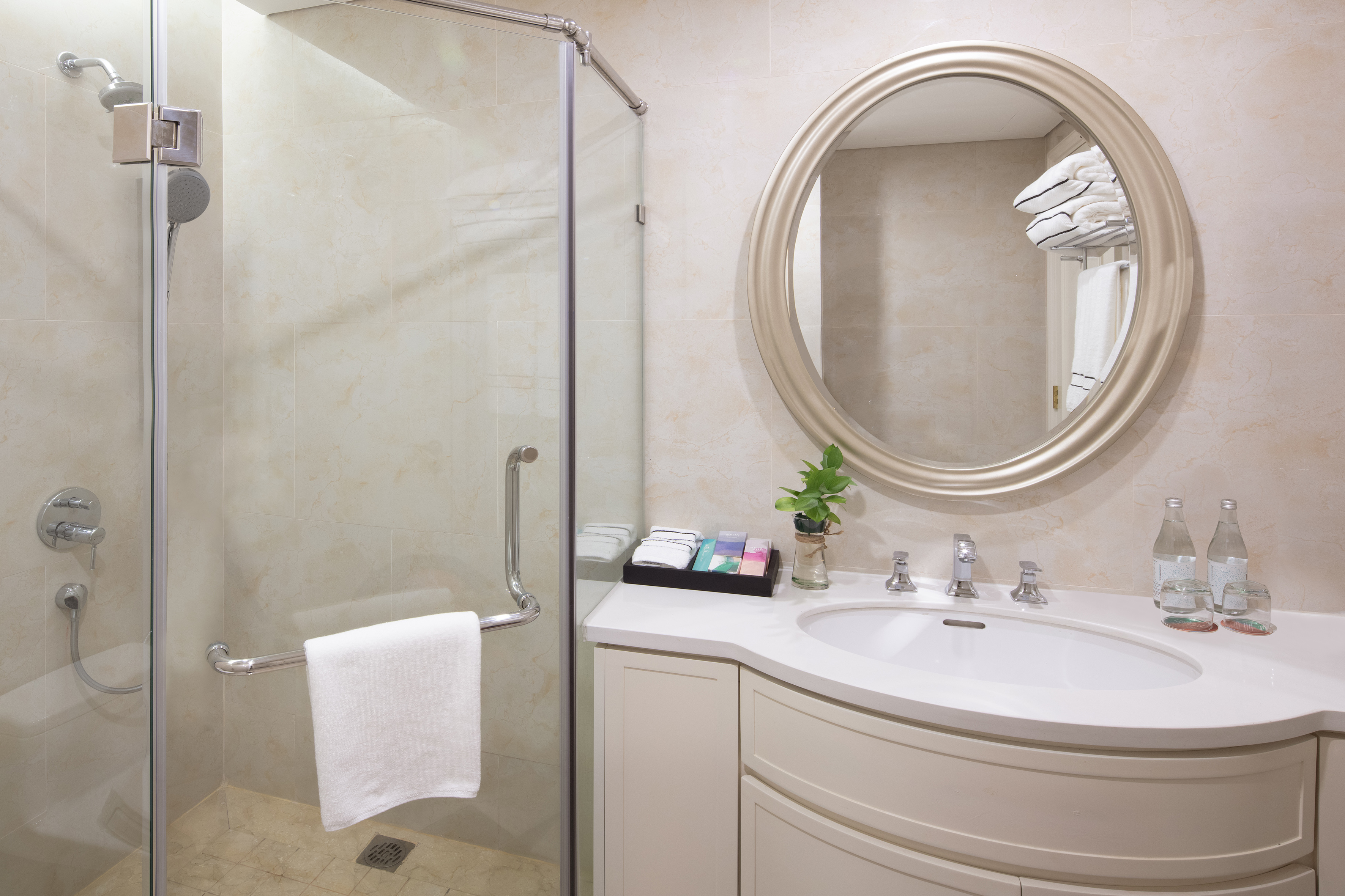 Modern hotel bathroom with glass shower, vanity, oval mirror, and amenities.