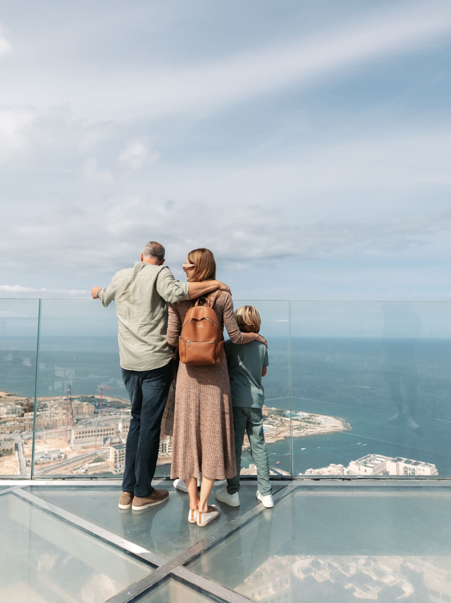 Family looking at panoramic ocean and city view from glass skydeck.