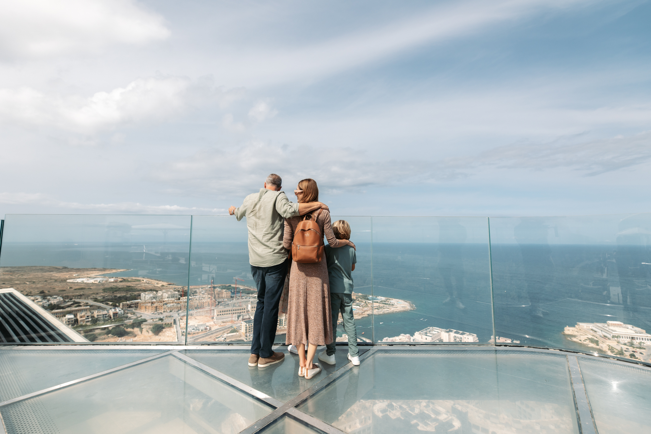 Family looking at panoramic ocean and city view from glass skydeck.