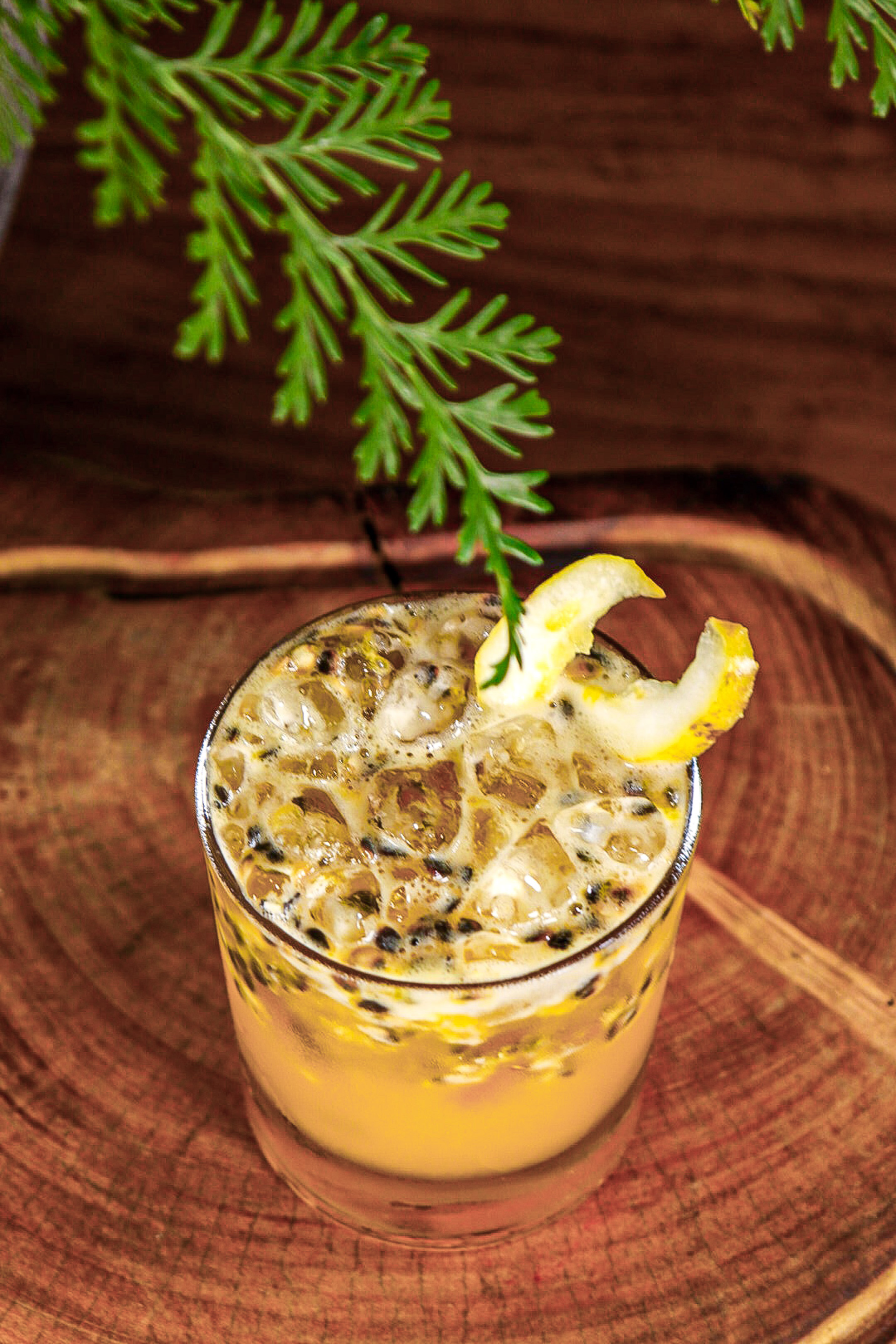 Passion fruit cocktail with ice, lemon garnish, on a rustic wood surface.