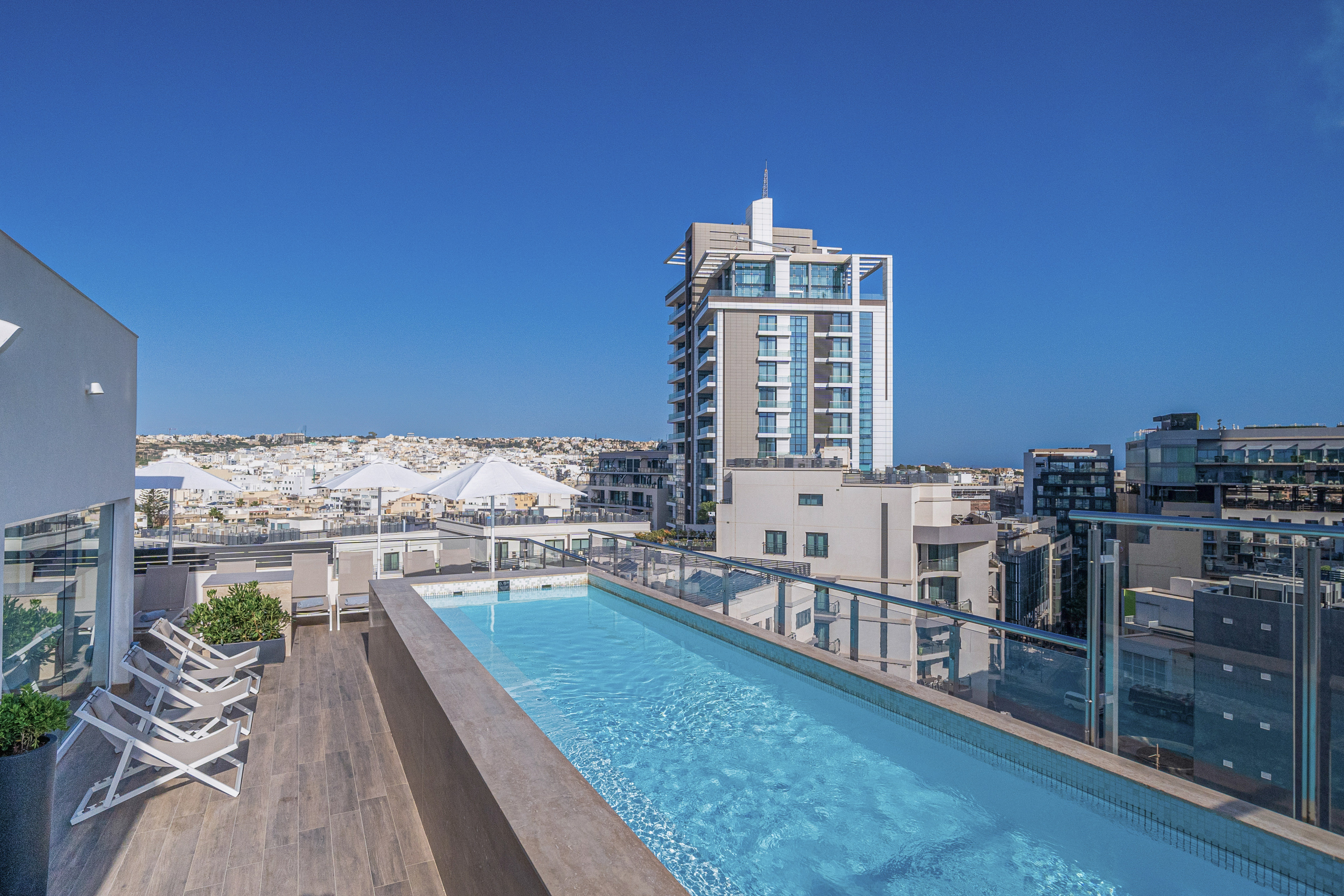 Modern rooftop pool with city view, lounge chairs, and tall buildings.