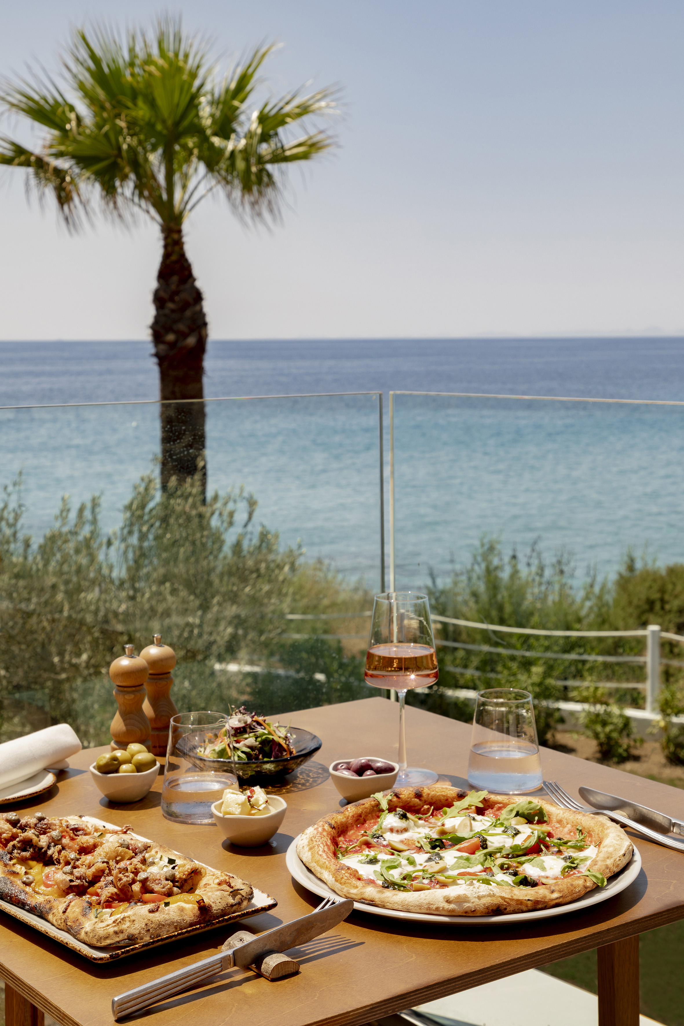Mediterranean dining: pizzas, salad, wine on ocean view terrace.