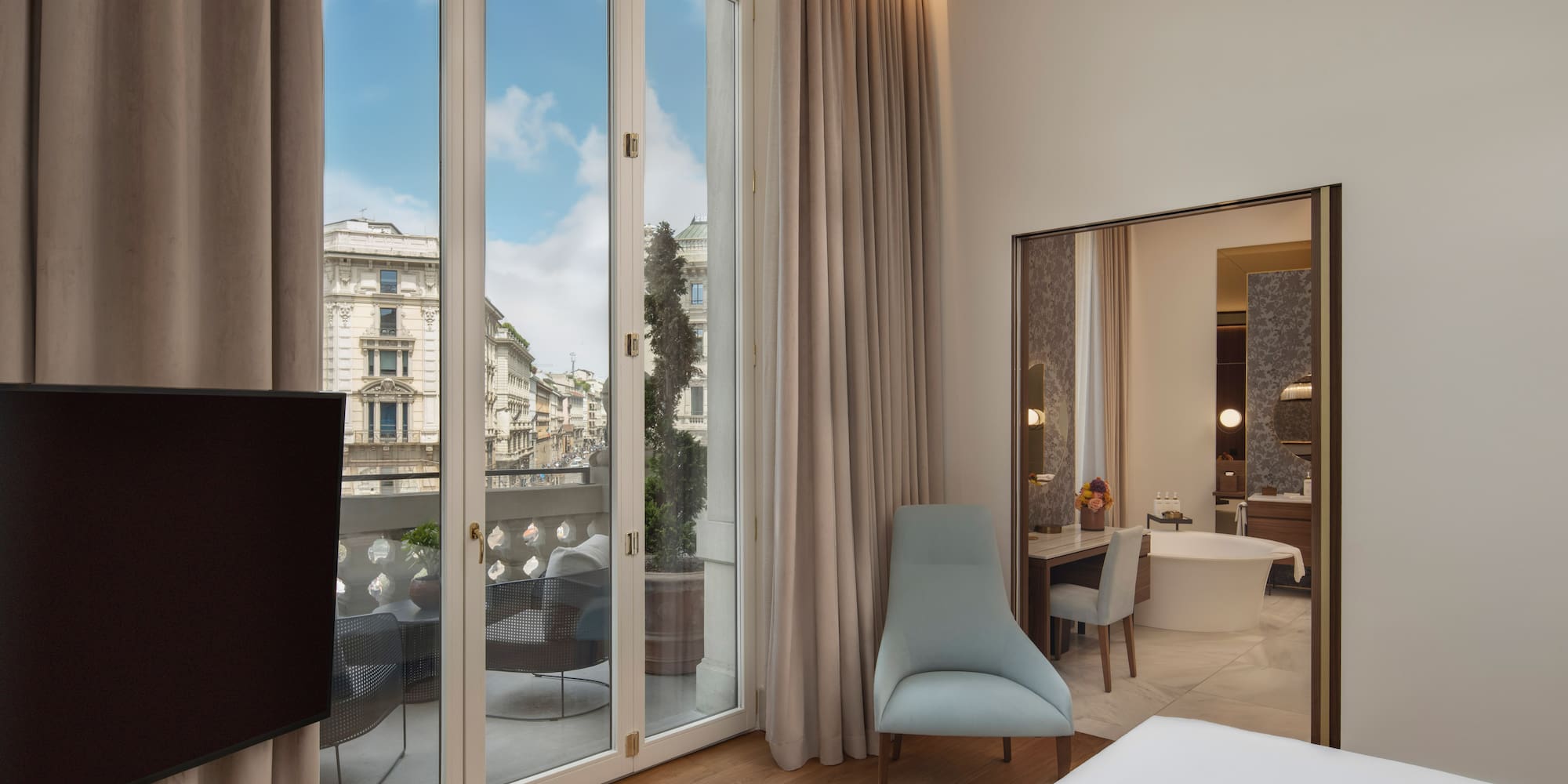 Modern hotel bedroom with balcony, city view, and adjoining bathroom.