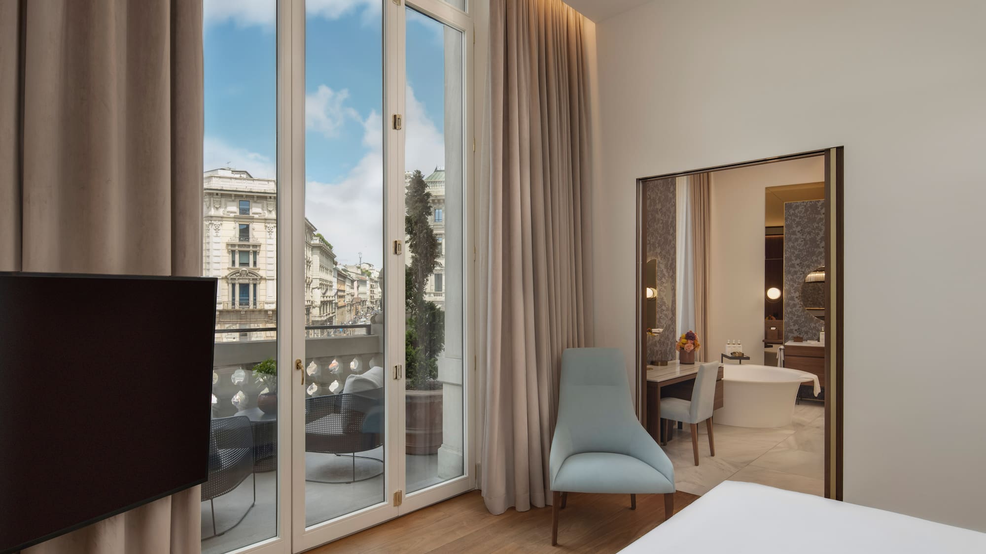 Modern hotel bedroom with balcony, city view, and adjoining bathroom.