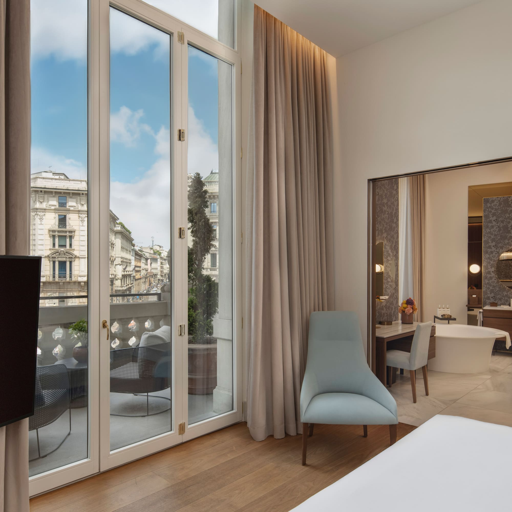 Modern hotel bedroom with balcony, city view, and adjoining bathroom.
