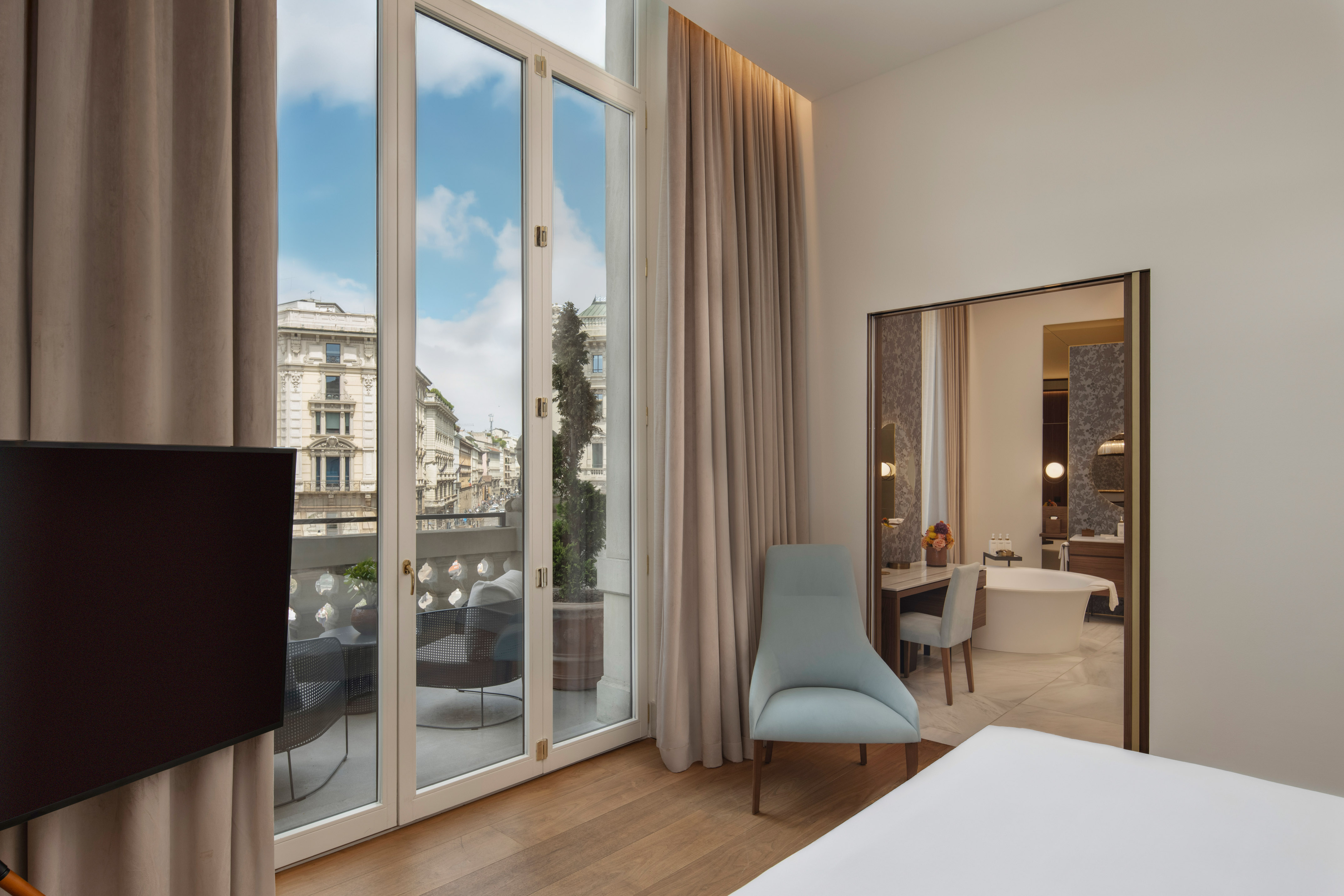 Modern hotel bedroom with balcony, city view, and adjoining bathroom.