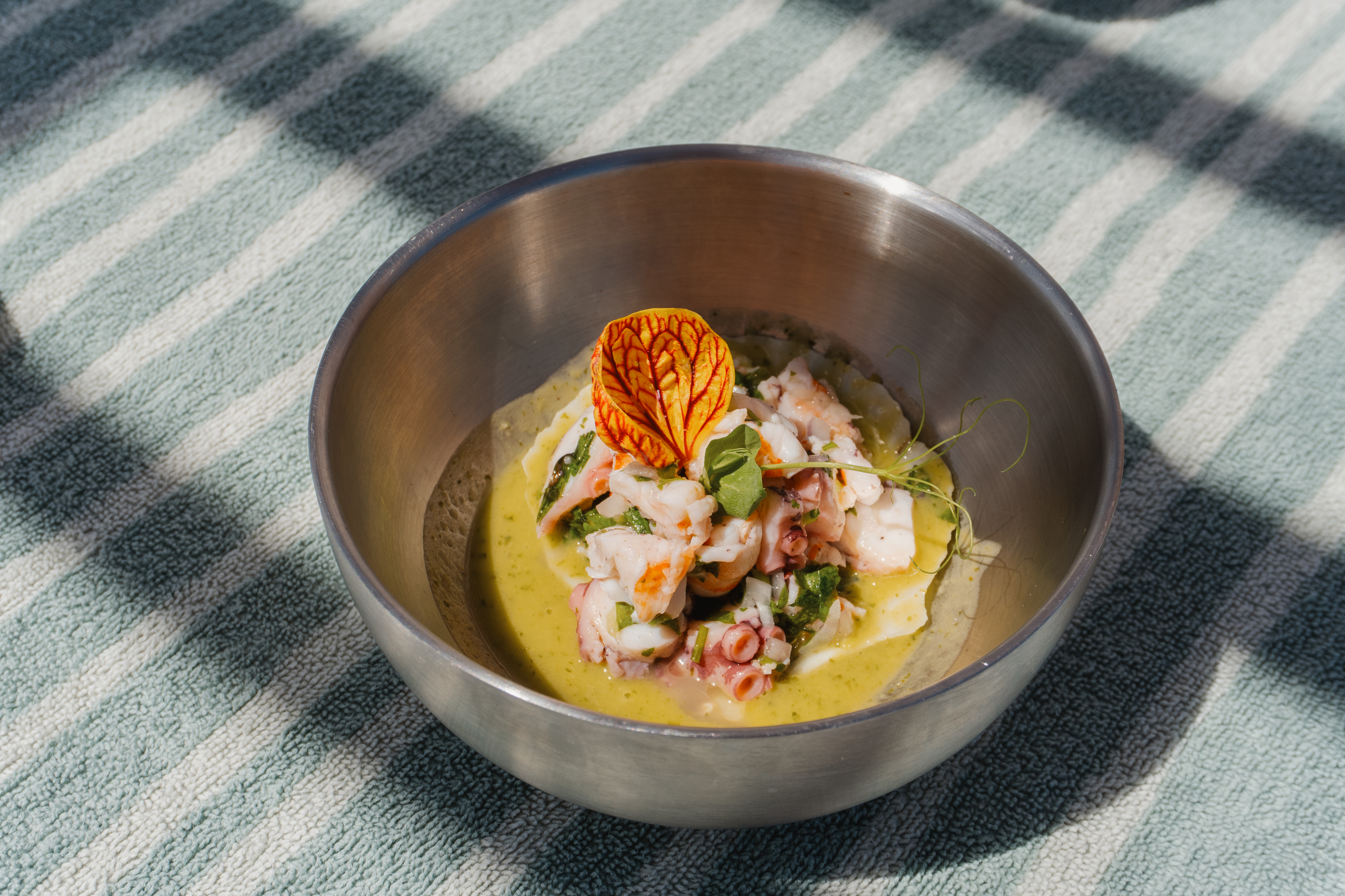 Shrimp and octopus ceviche, garnished, in a metal bowl on a striped towel.