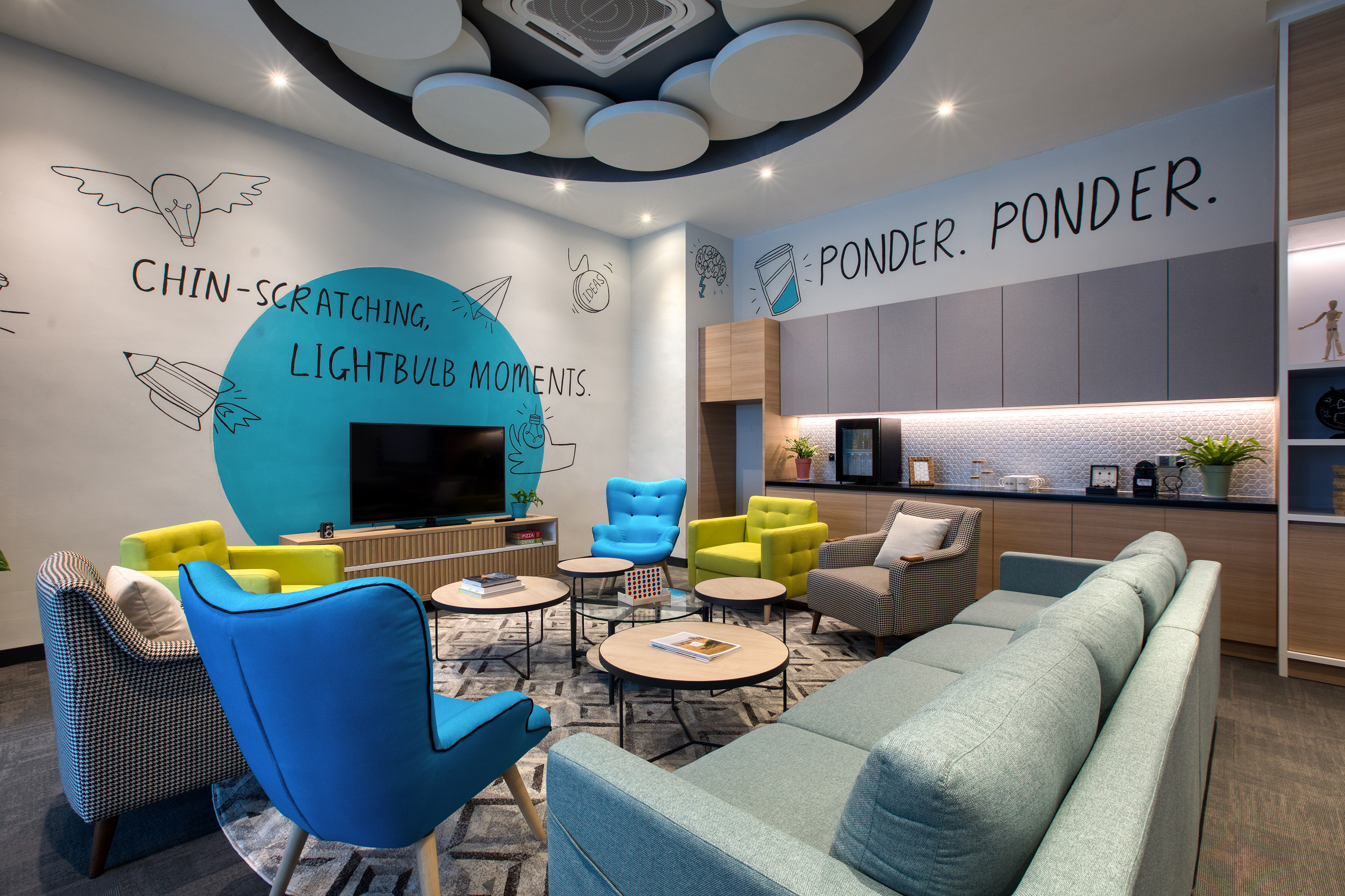 Vibrant modern office lounge with colorful seating, creative murals, and kitchenette.