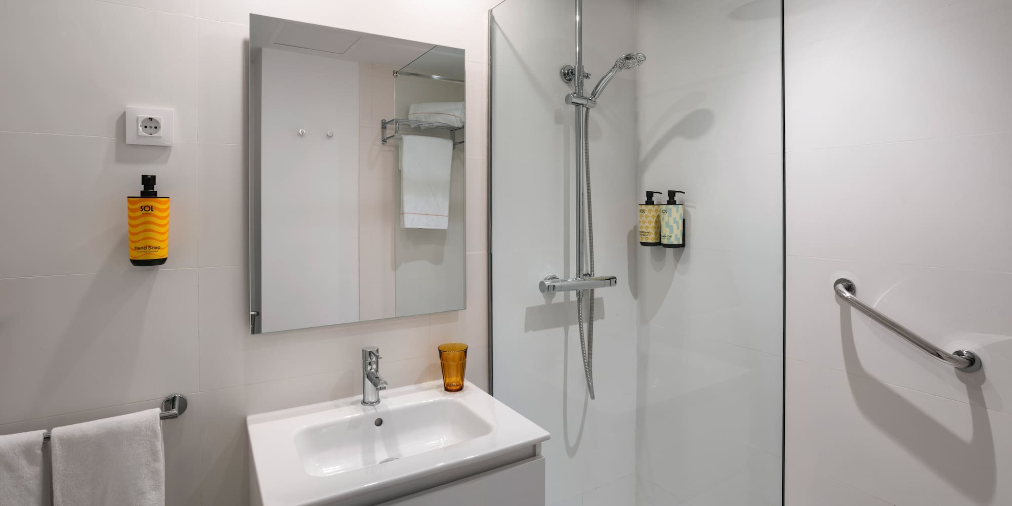 White tiled modern bathroom with vanity, mirror, walk-in shower, and grab bar.
