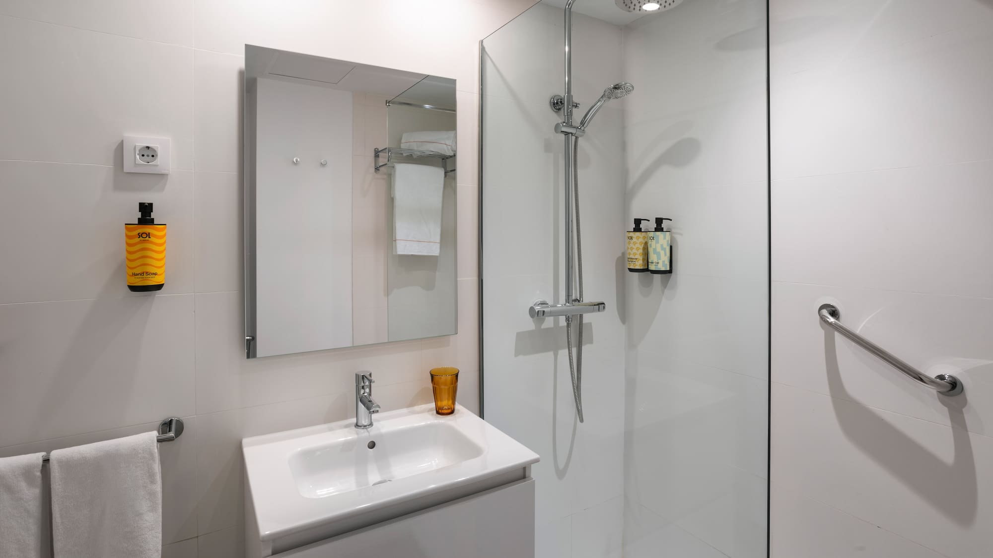 White tiled modern bathroom with vanity, mirror, walk-in shower, and grab bar.