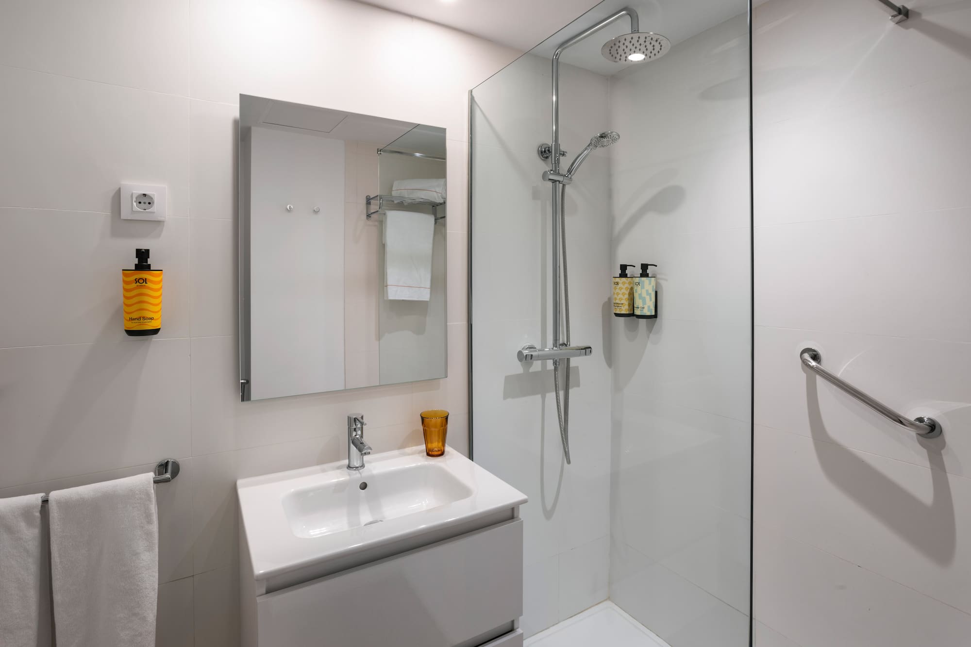 Clean, modern hotel bathroom with sink, mirror, and glass walk-in shower.