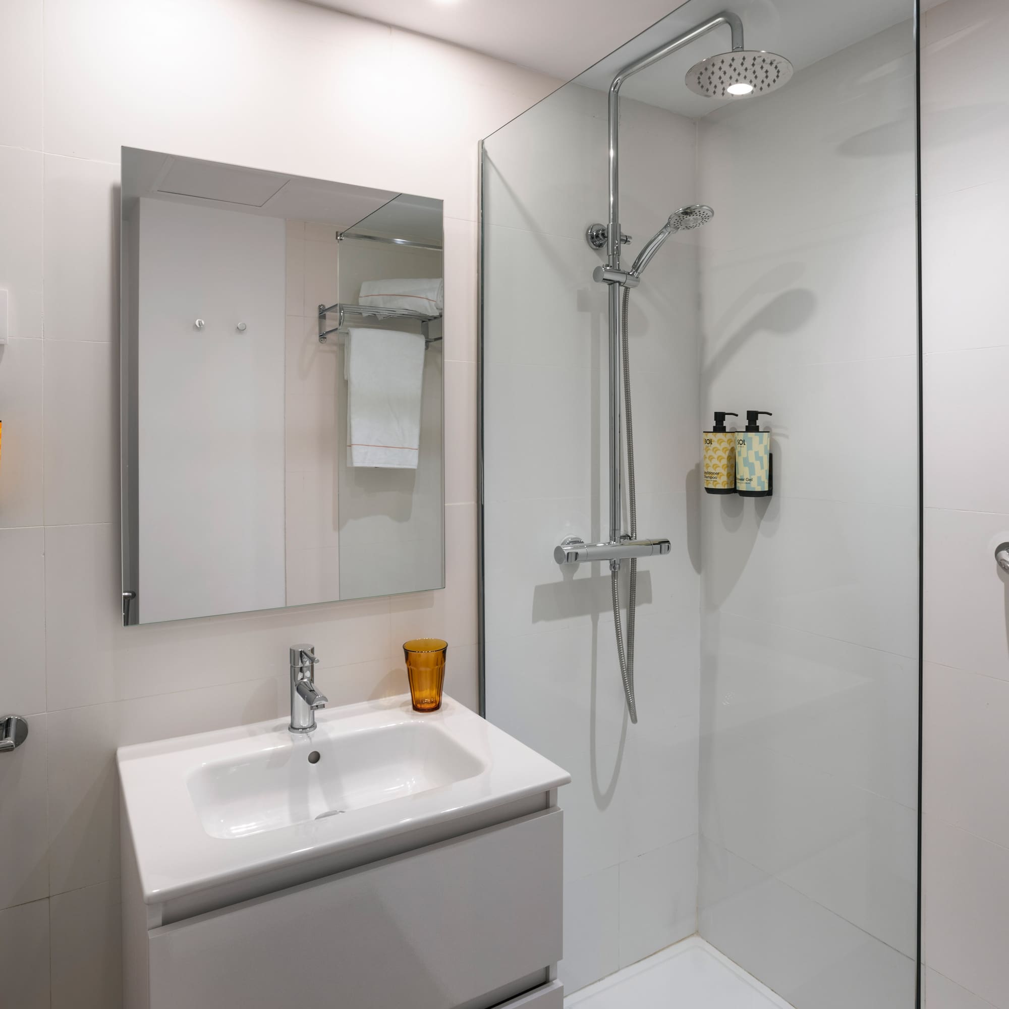 White tiled modern bathroom with vanity, mirror, walk-in shower, and grab bar.