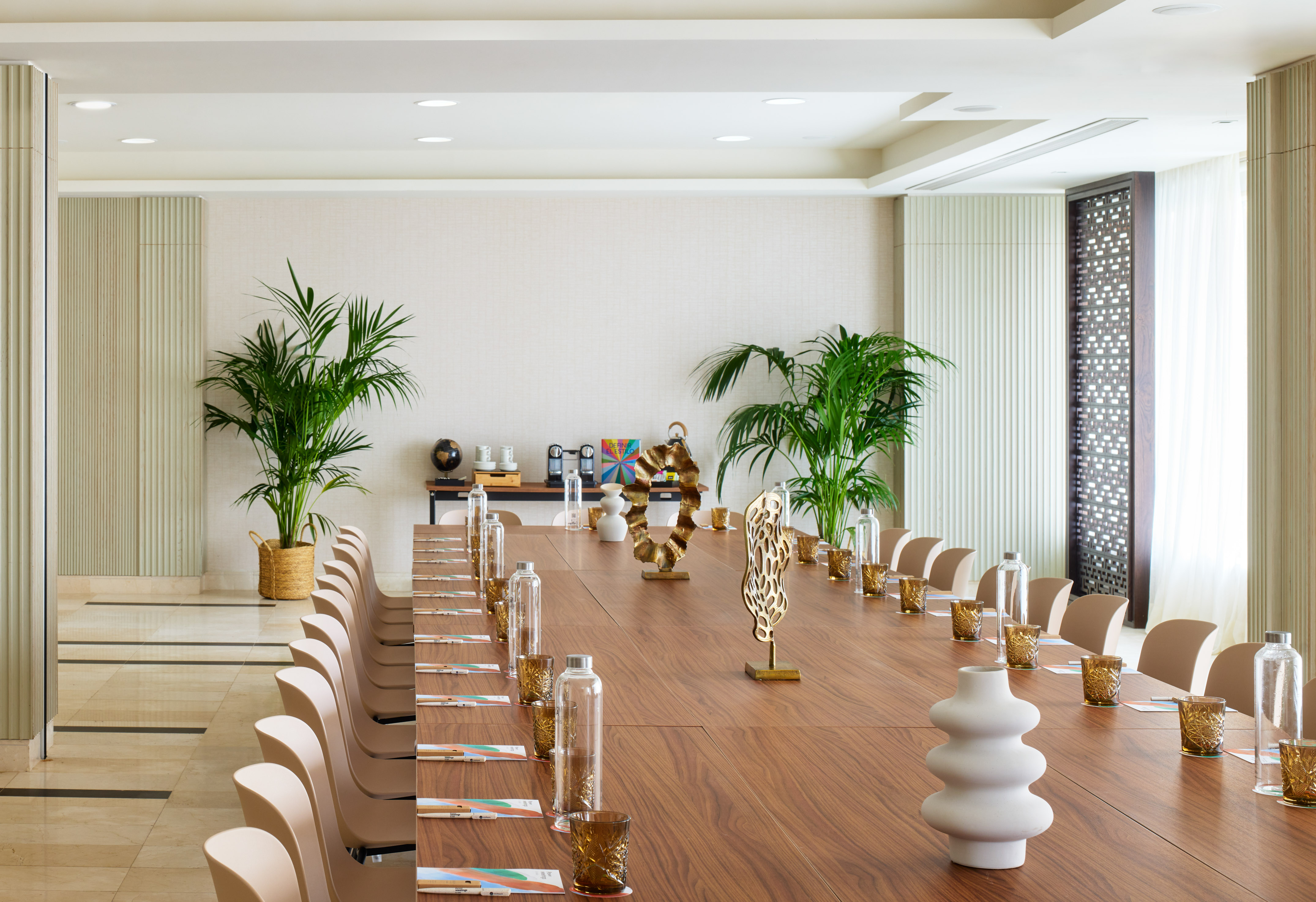 Modern conference room with long wooden table, beige chairs, and green plants.