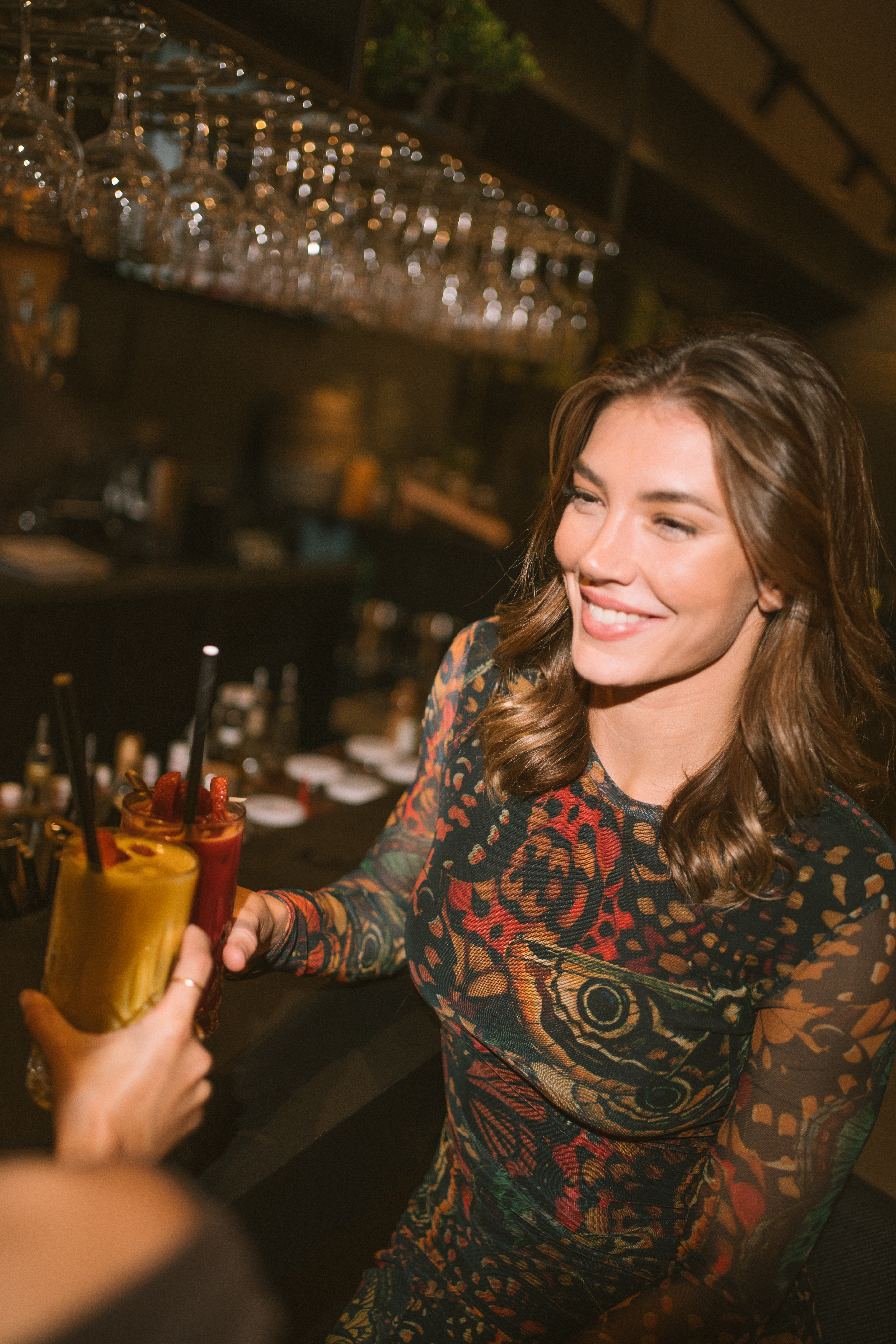 Smiling woman toasting colorful cocktails at a chic bar.