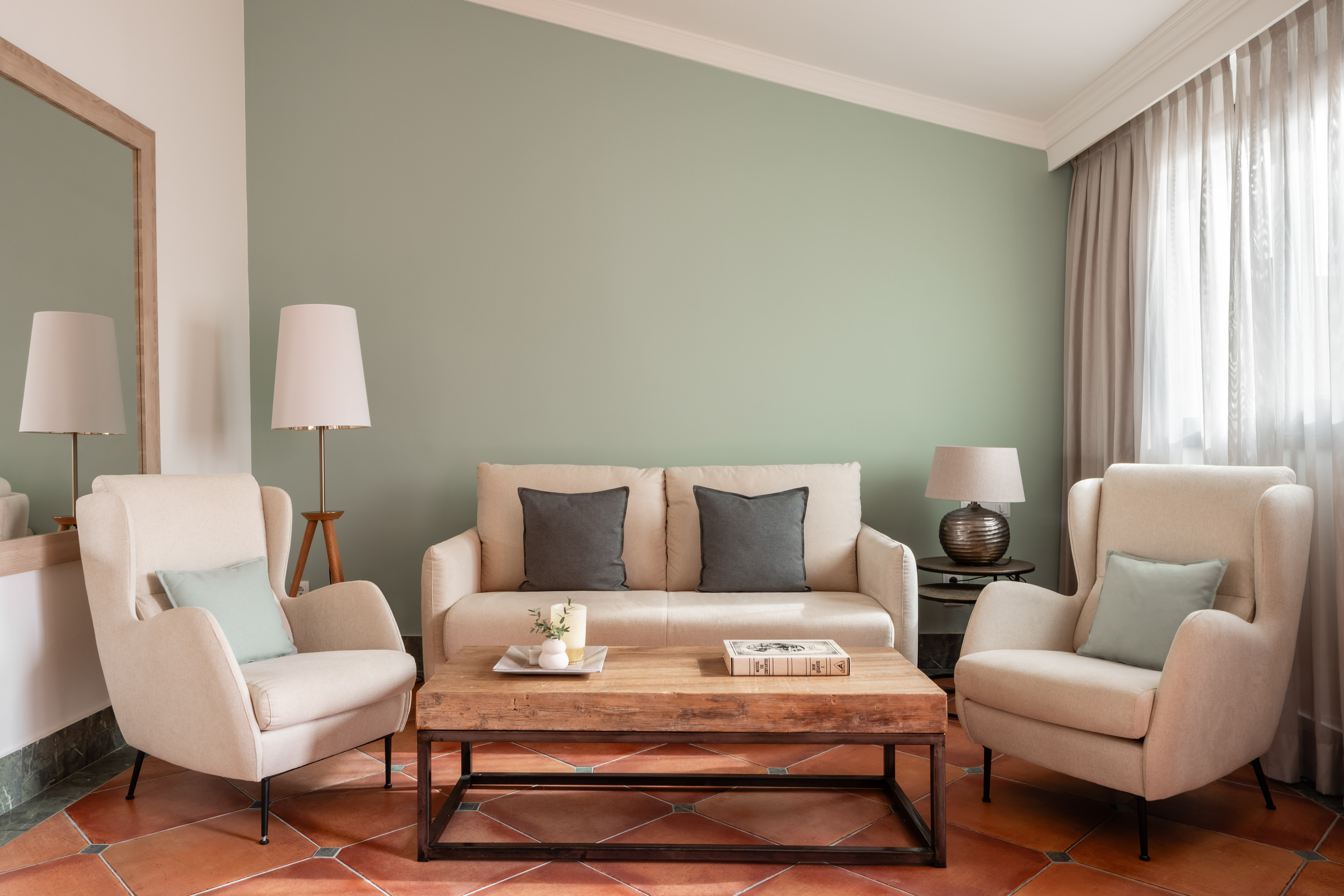 Cream living room furniture, wood coffee table, sage green wall, terracotta floor.