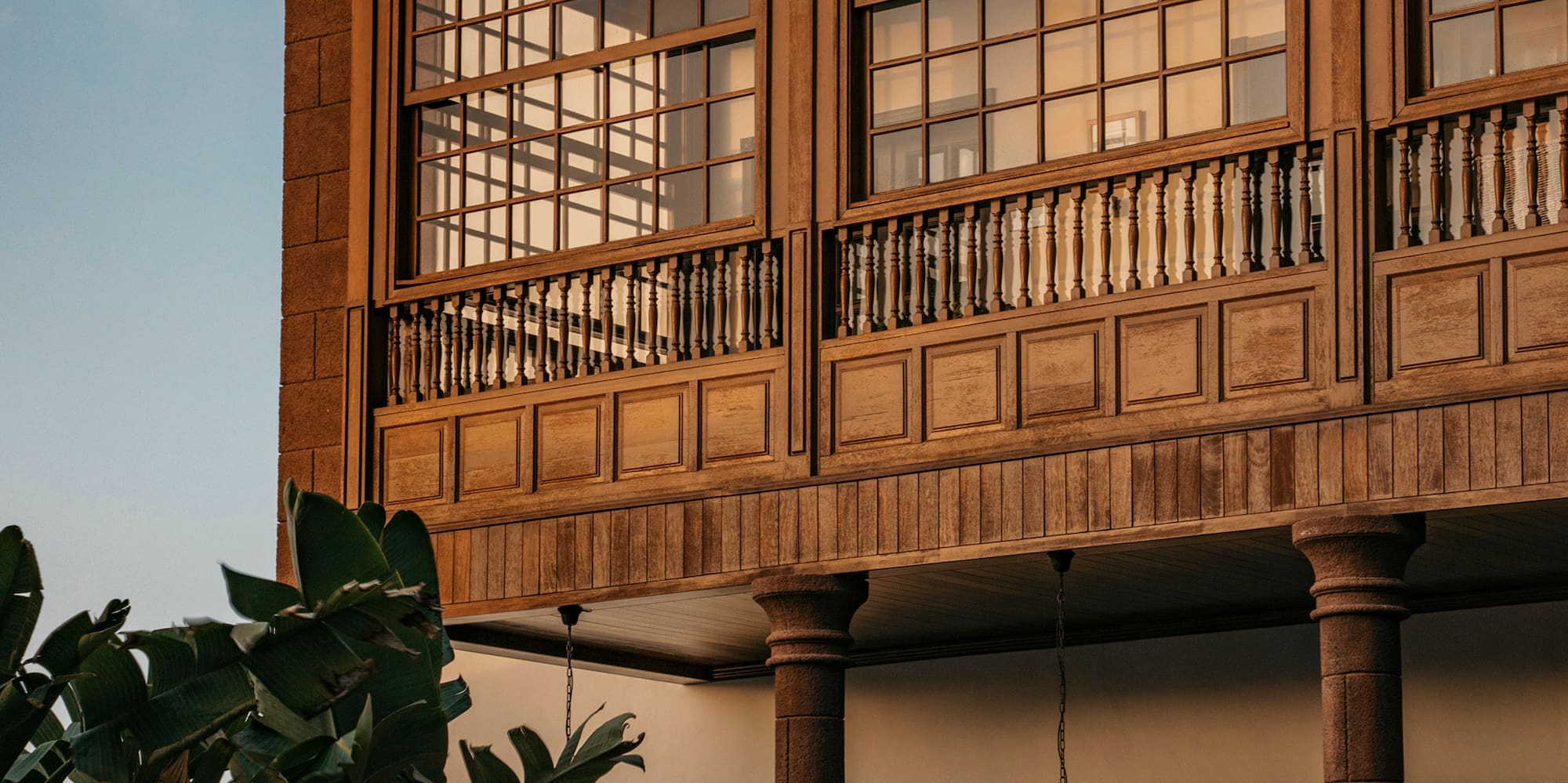 Wooden building facade with large windows, balcony, tiled roof, and lush plants.