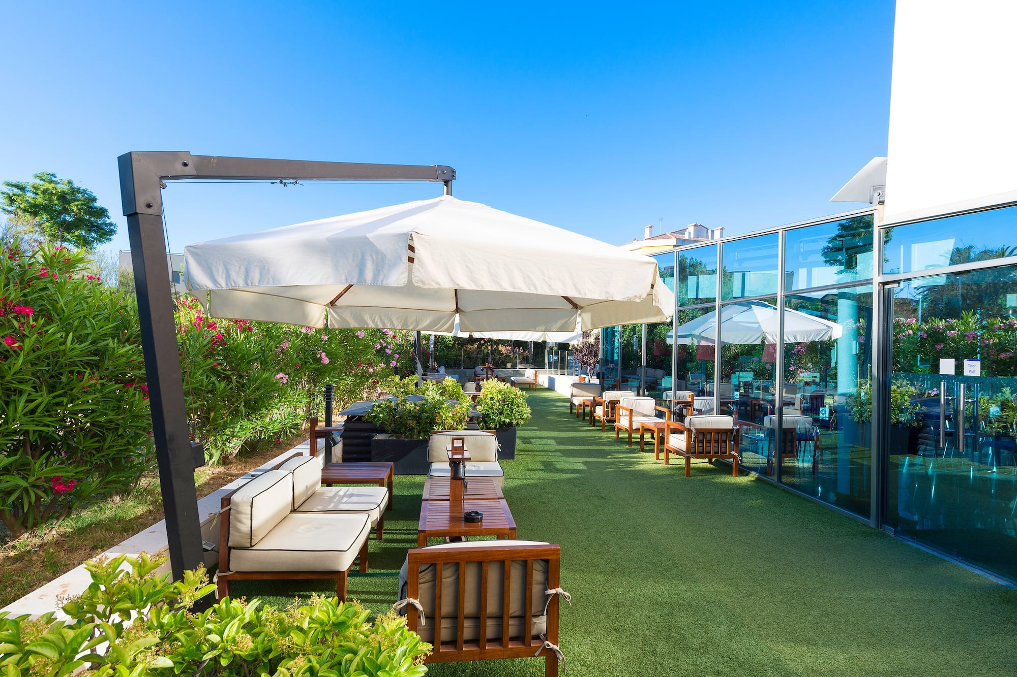 Outdoor cafe patio with green turf, white umbrellas, and glass facade building.