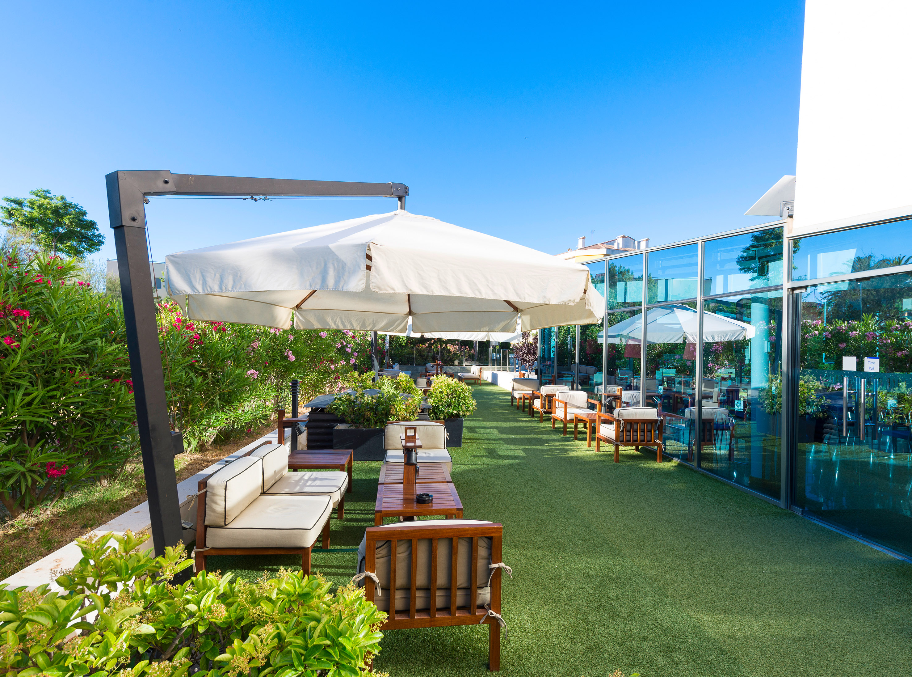 Outdoor cafe patio with green turf, white umbrellas, and glass facade building.