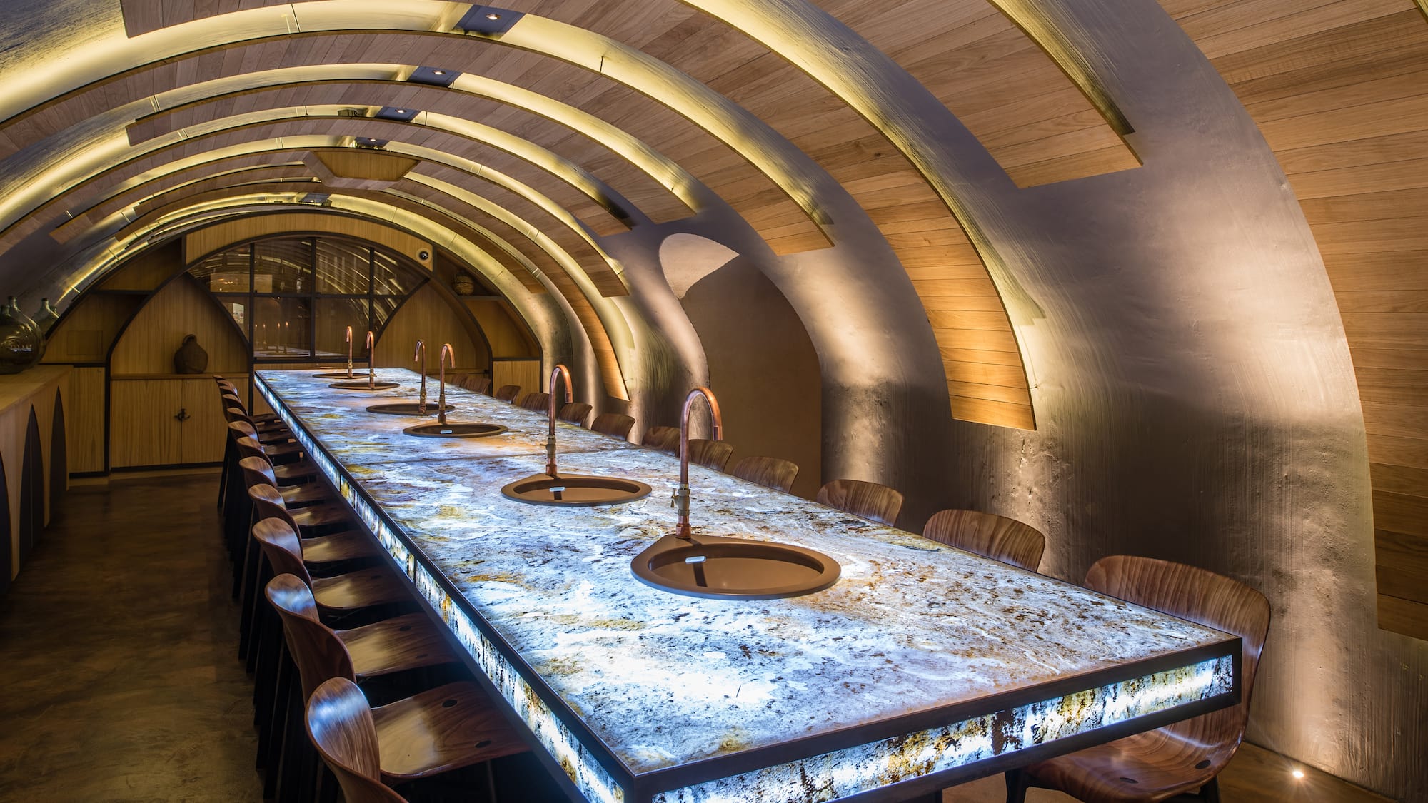 a long table with sinks and chairs in a room with arched ceiling