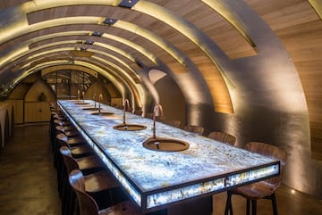 a long table with sinks and chairs in a room with arched ceiling