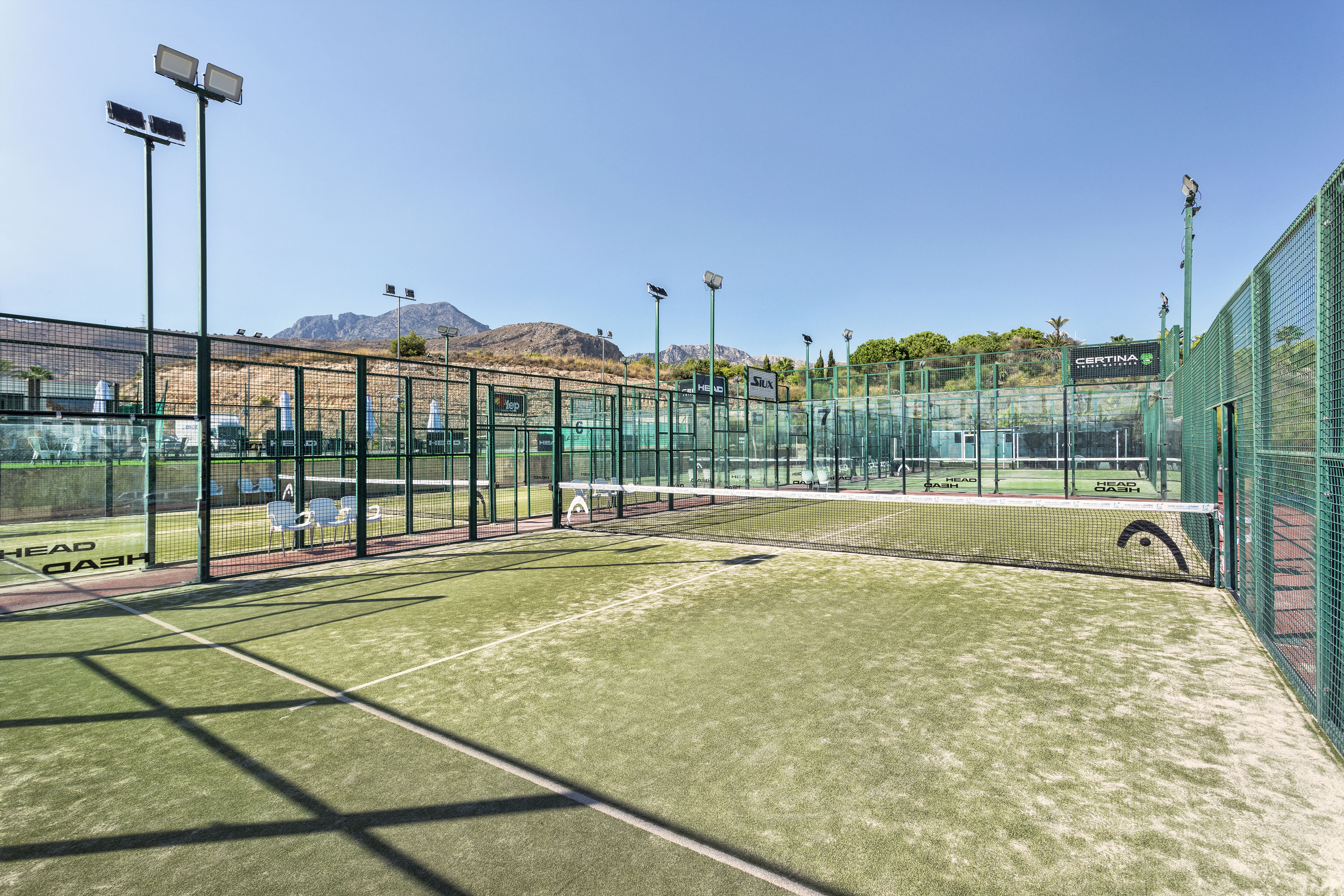 Multiple outdoor padel courts with green turf, nets, fences, and distant mountains.