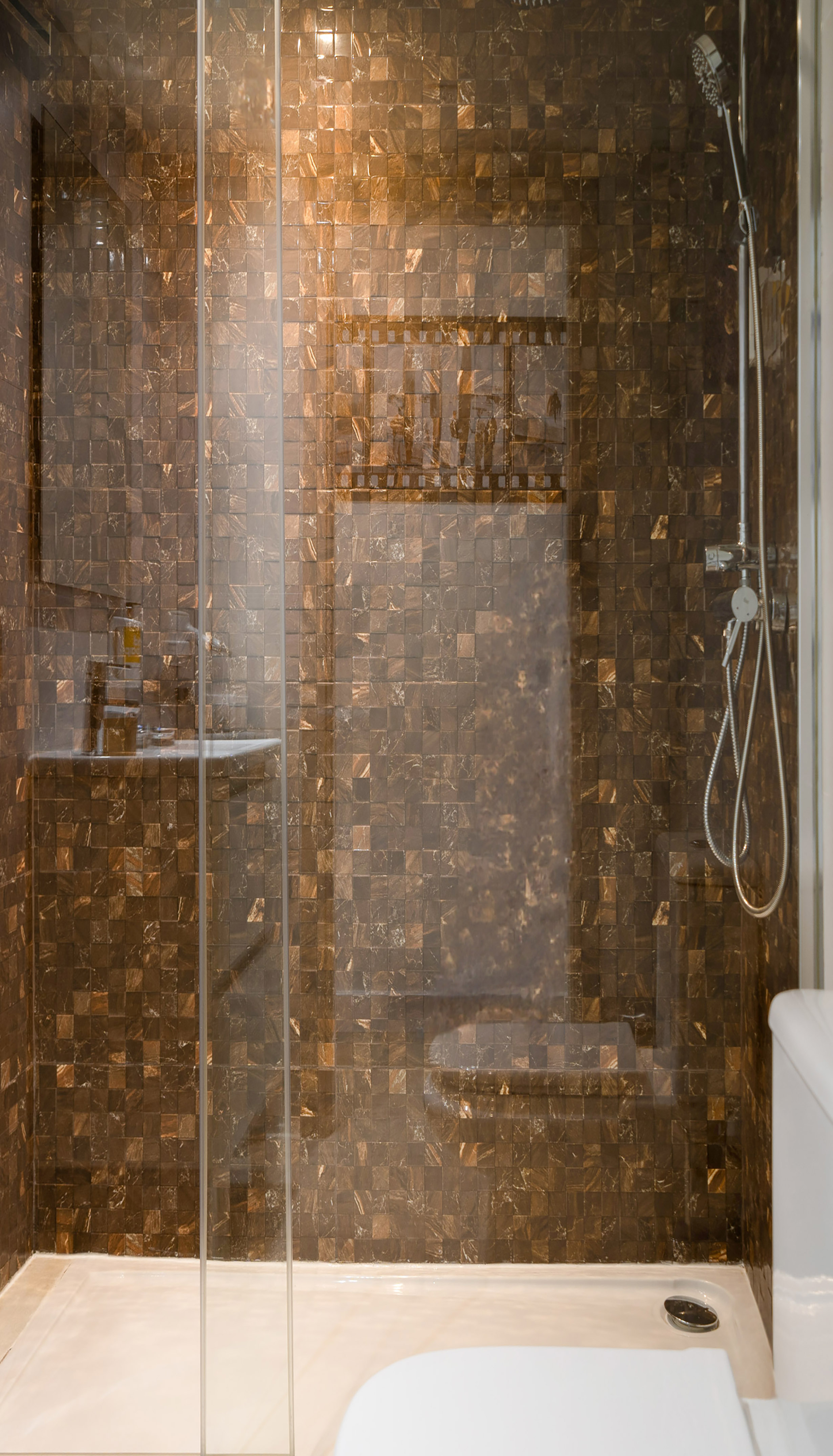 Modern brown mosaic tiled shower with glass enclosure and shower head.