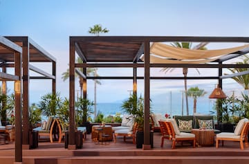 a patio with chairs and tables on a deck overlooking the ocean