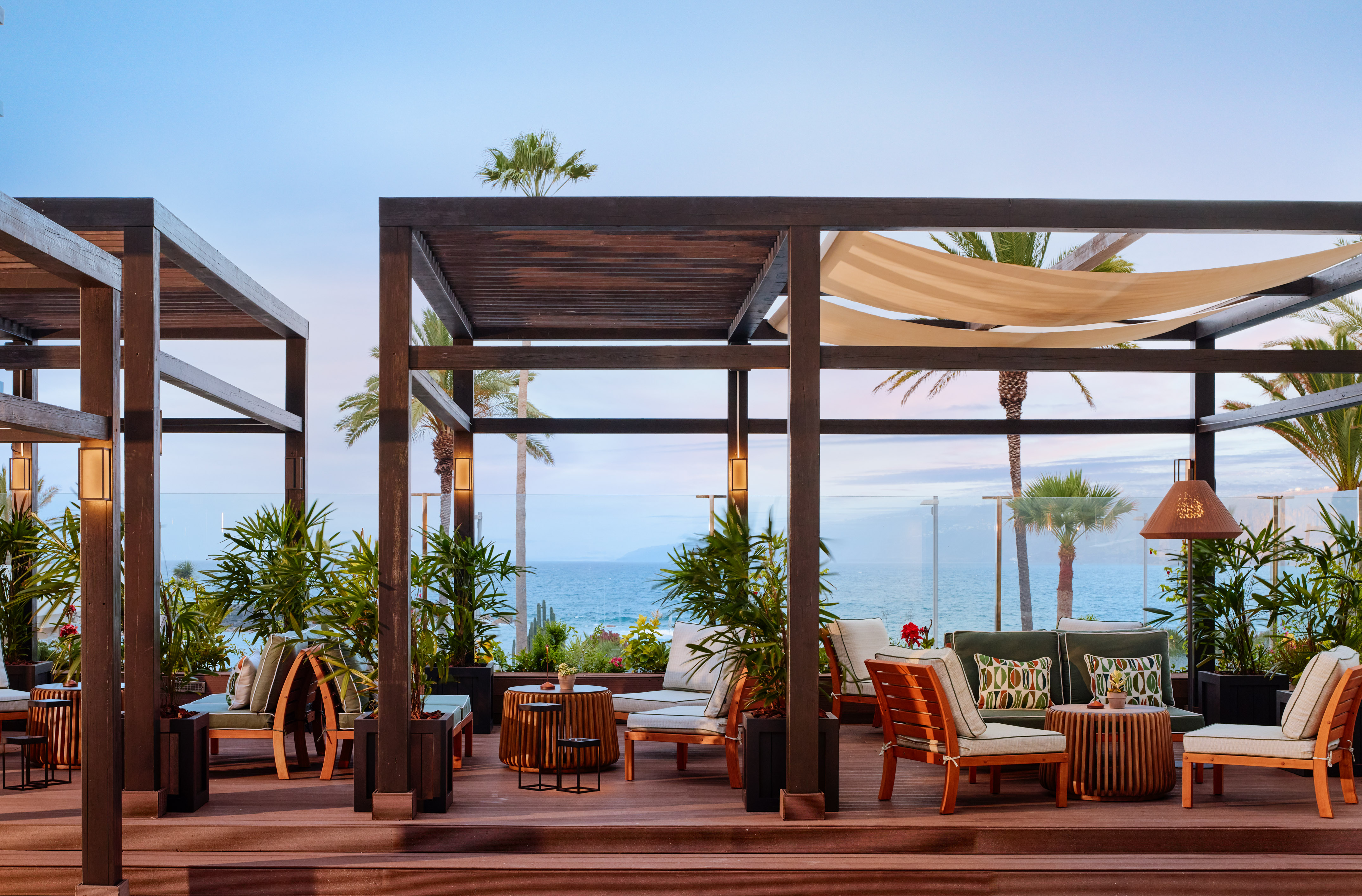 a patio with chairs and tables on a deck overlooking the ocean