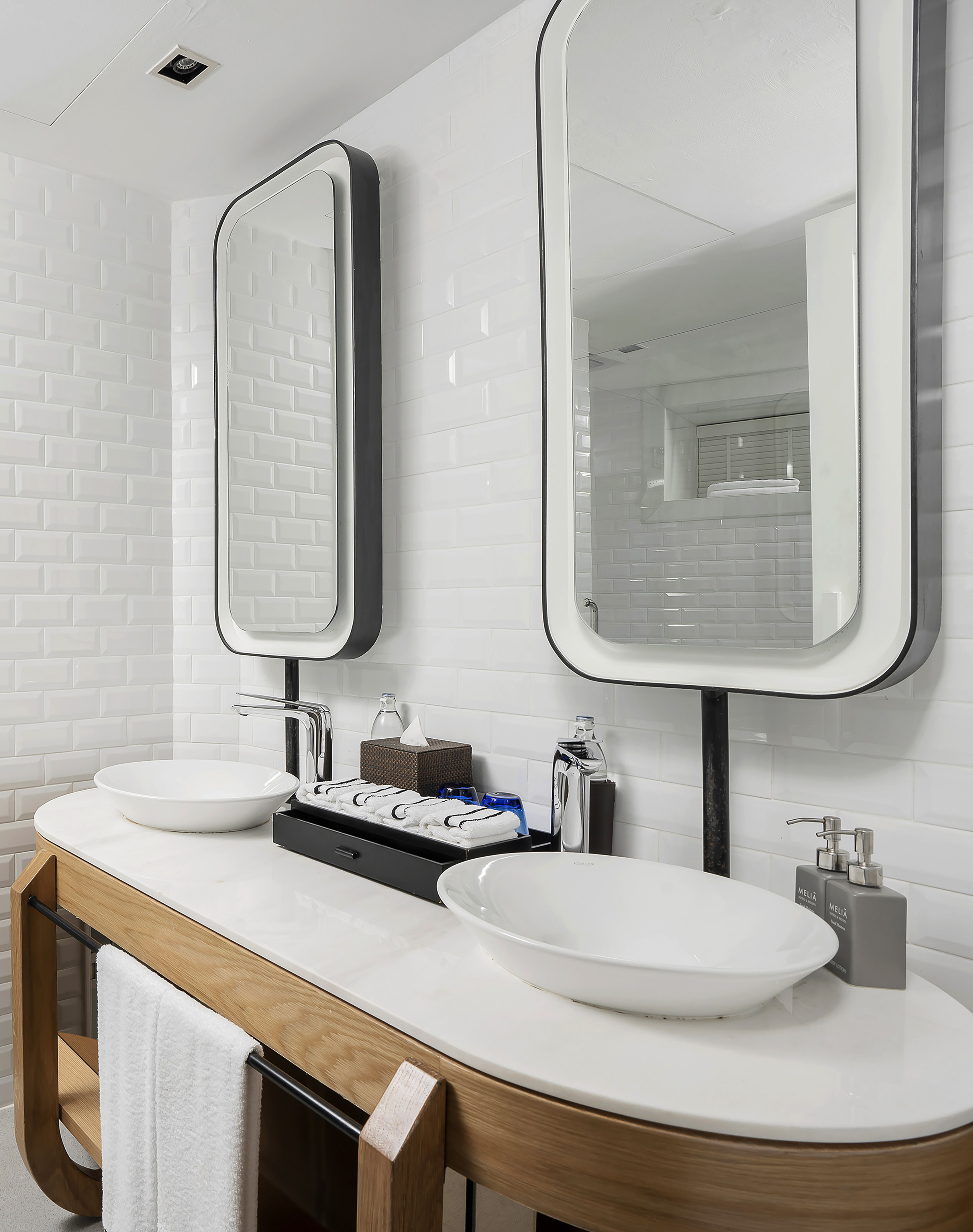 Modern bathroom with dual vessel sinks, black-framed mirrors, and white subway tiles.