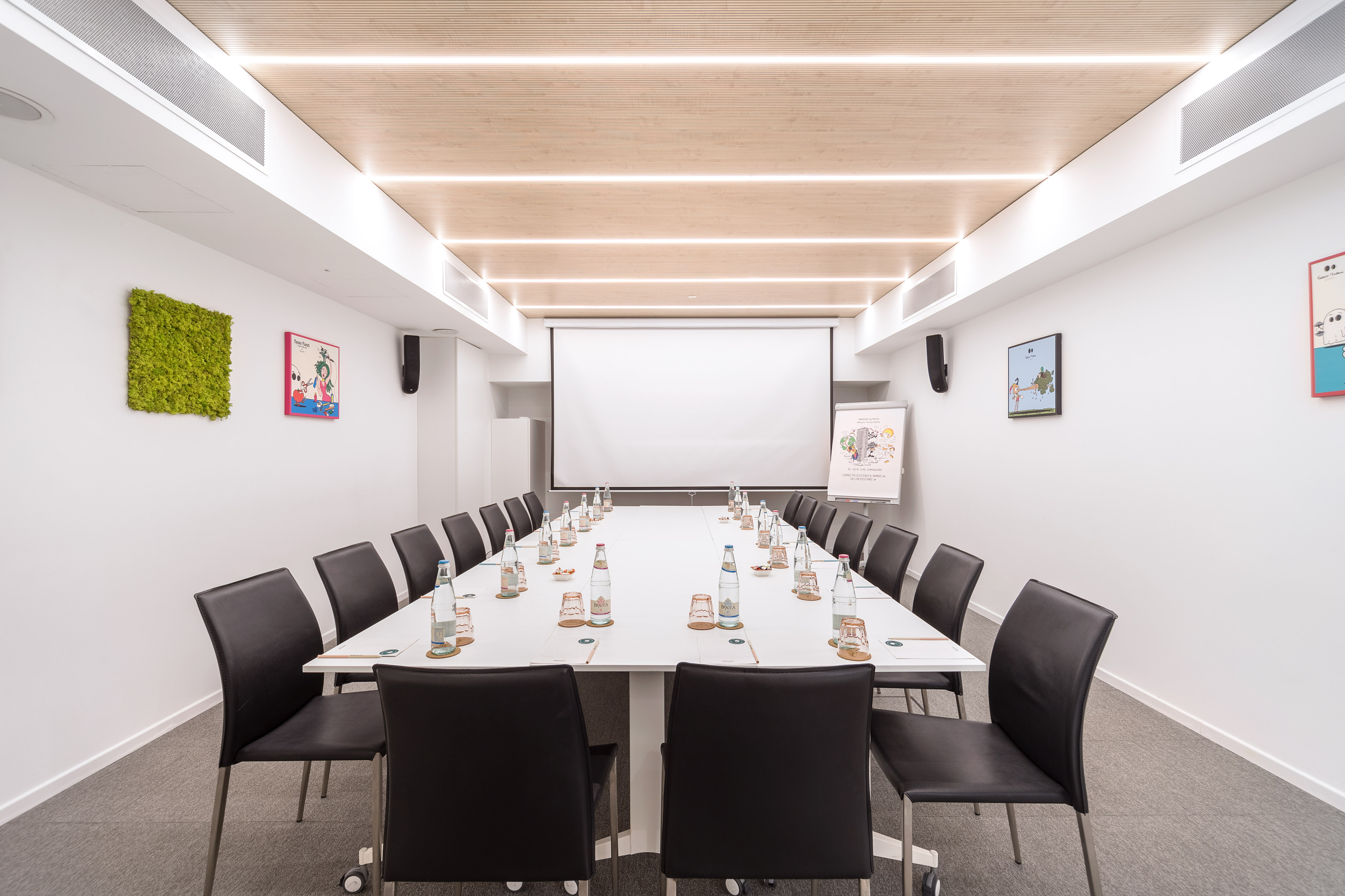 Modern meeting room with U-shaped table, projector screen, wooden ceiling.