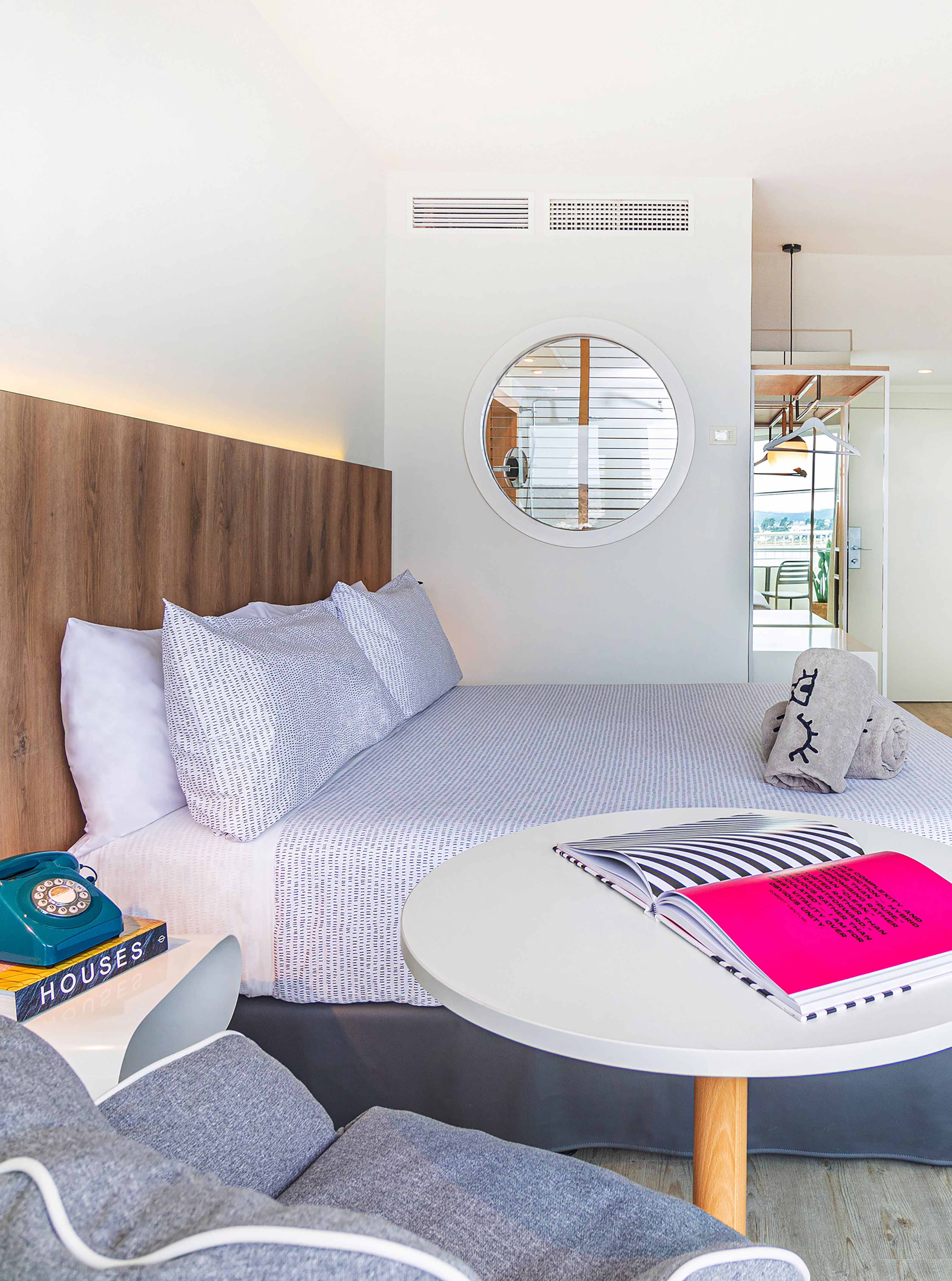 Modern hotel bedroom with patterned bedding, wooden headboard, and round mirror.