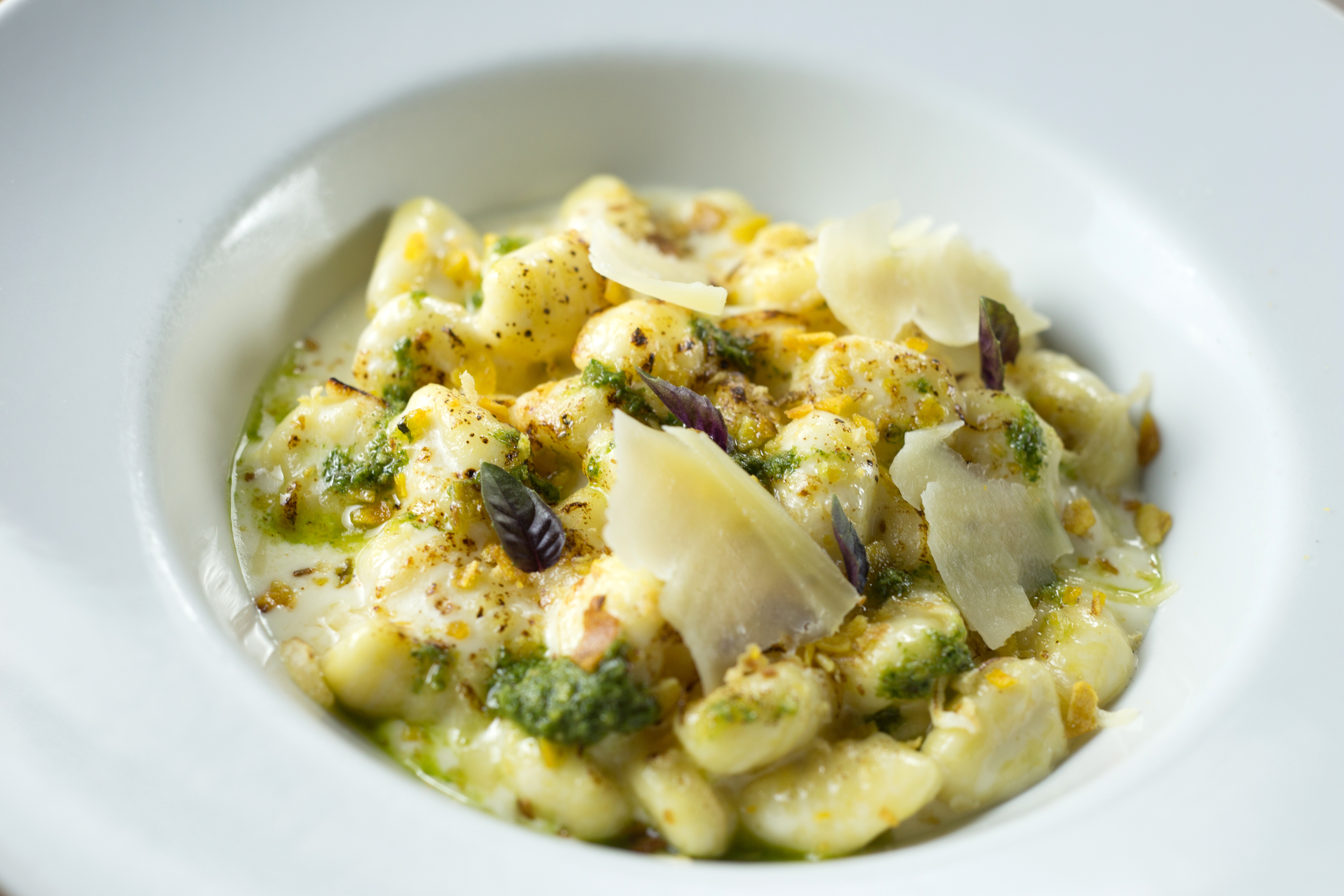 Creamy Italian gnocchi with pesto, shaved Parmesan, and basil.