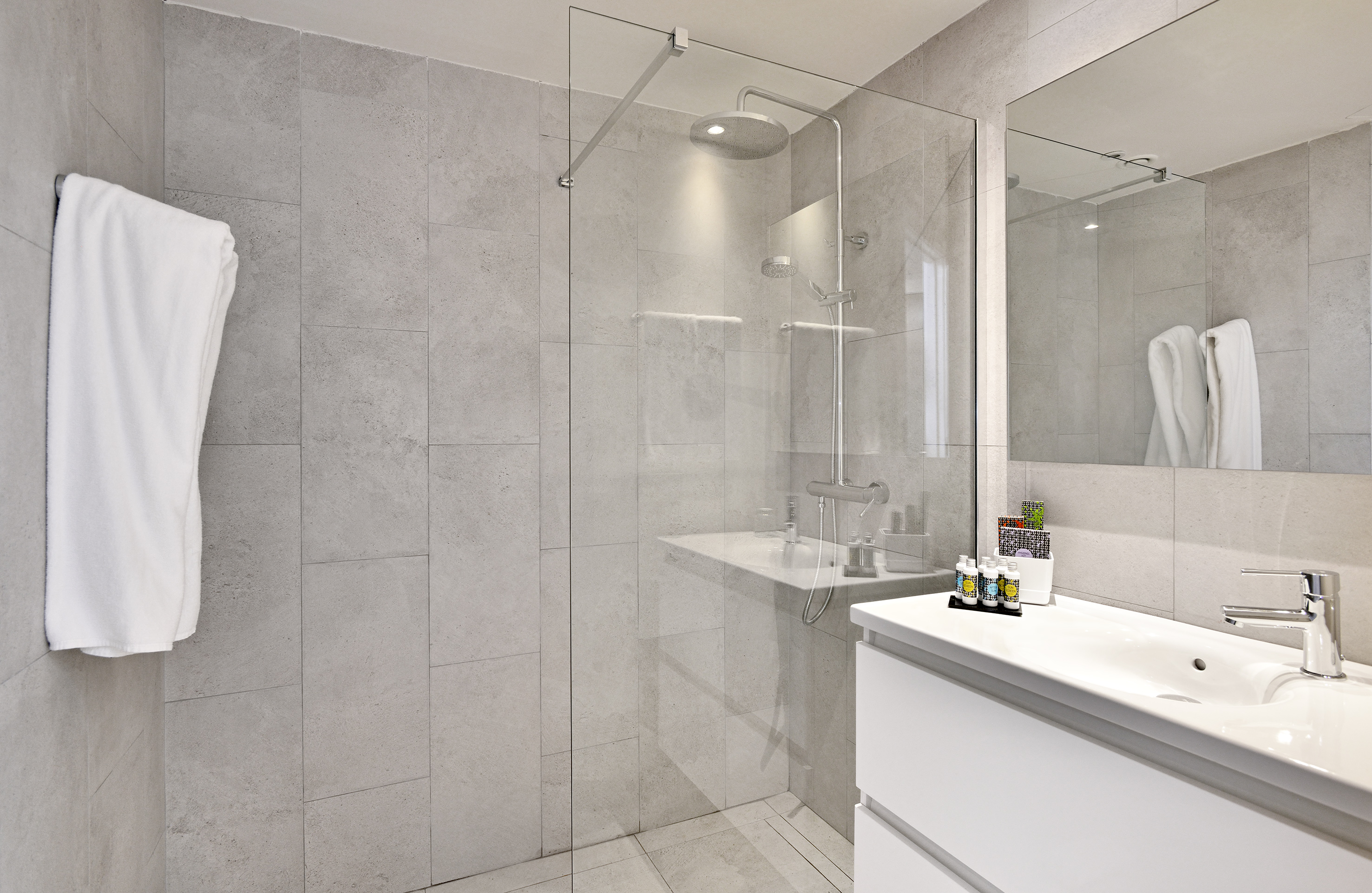 Modern bathroom with tiled walk-in shower, rain shower, and white vanity sink.