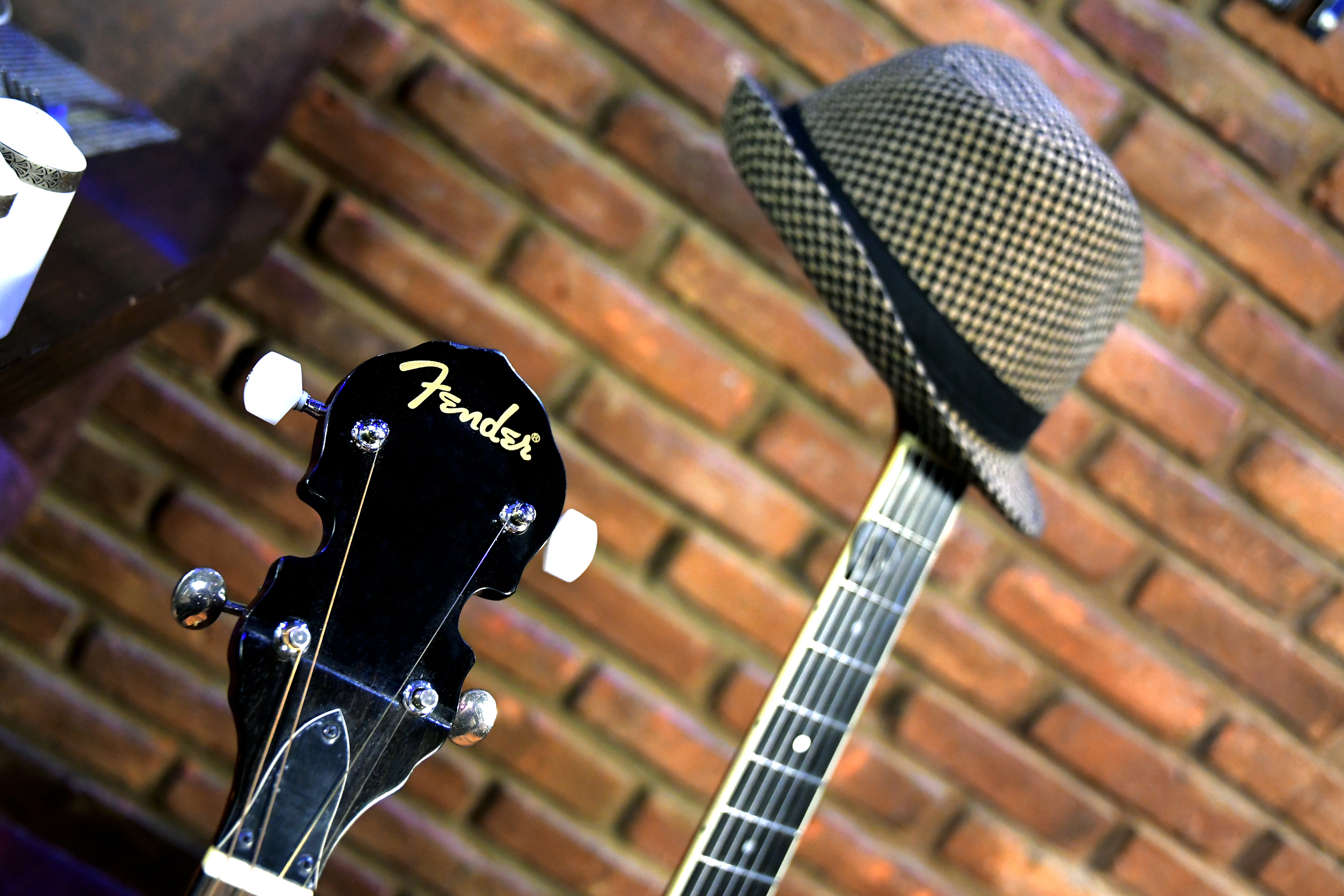 Fender guitar headstock, neck, and checkered fedora hat against a brick wall. - Jazz Voyeur Club - Melia Recoleta Plaza, Buenos Aires